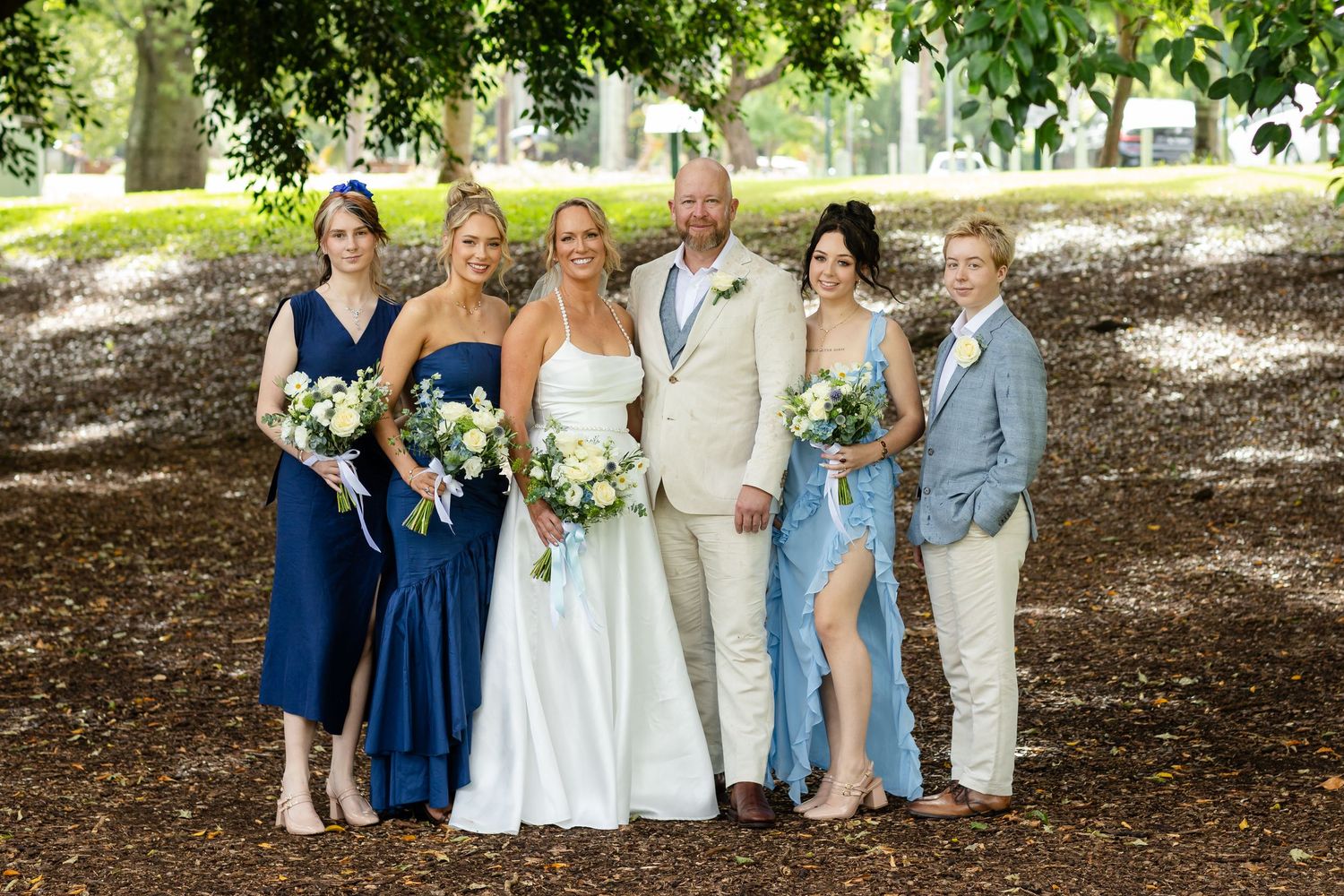 Wedding party stands under lush green trees for outdoor group photo.New farm park wedding photos in Brisbane