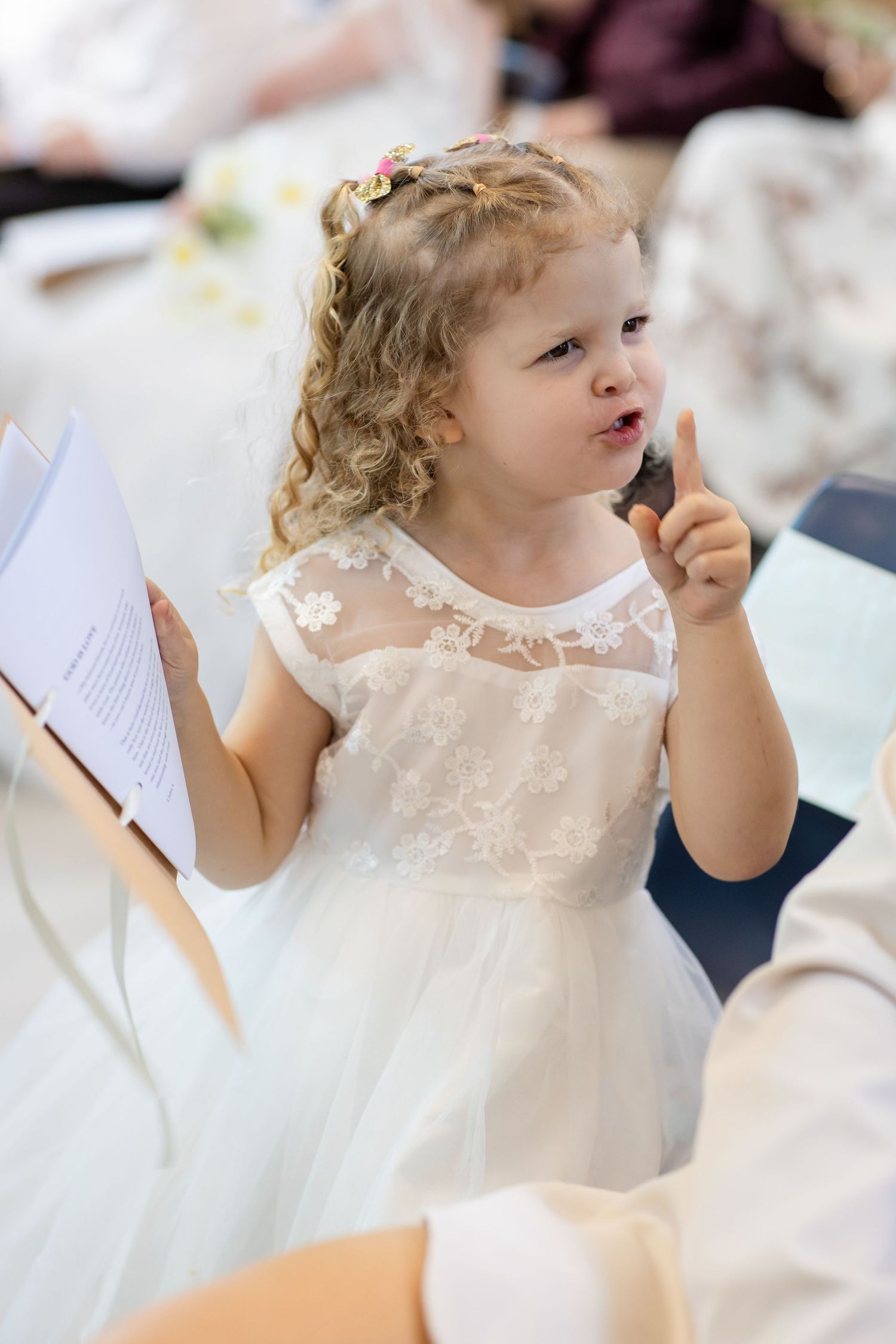 A flower girl in a white lace dress participates in the wedding ceremony.