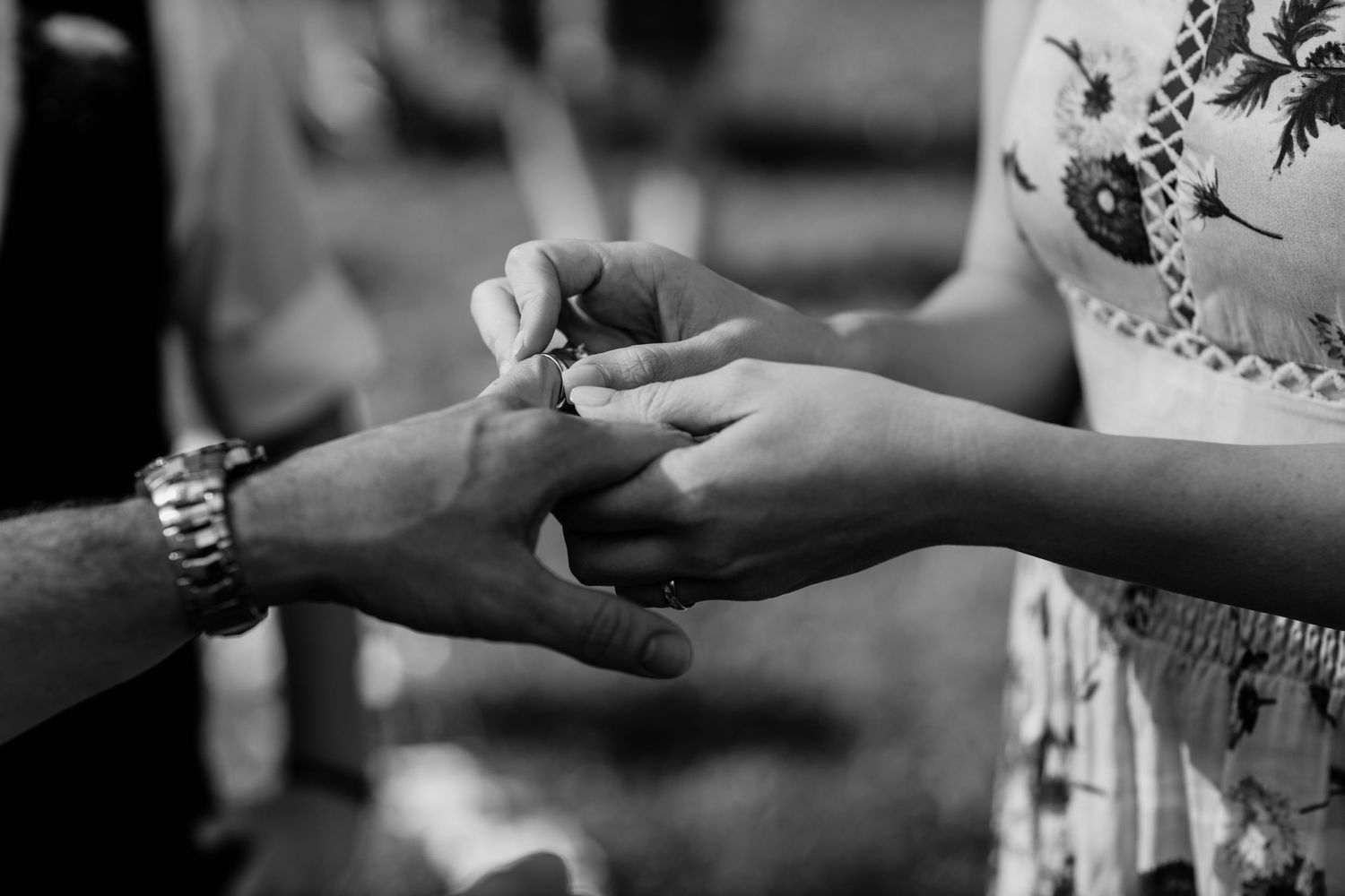 Black and white close-up of hands exchanging a ring during a ceremony.