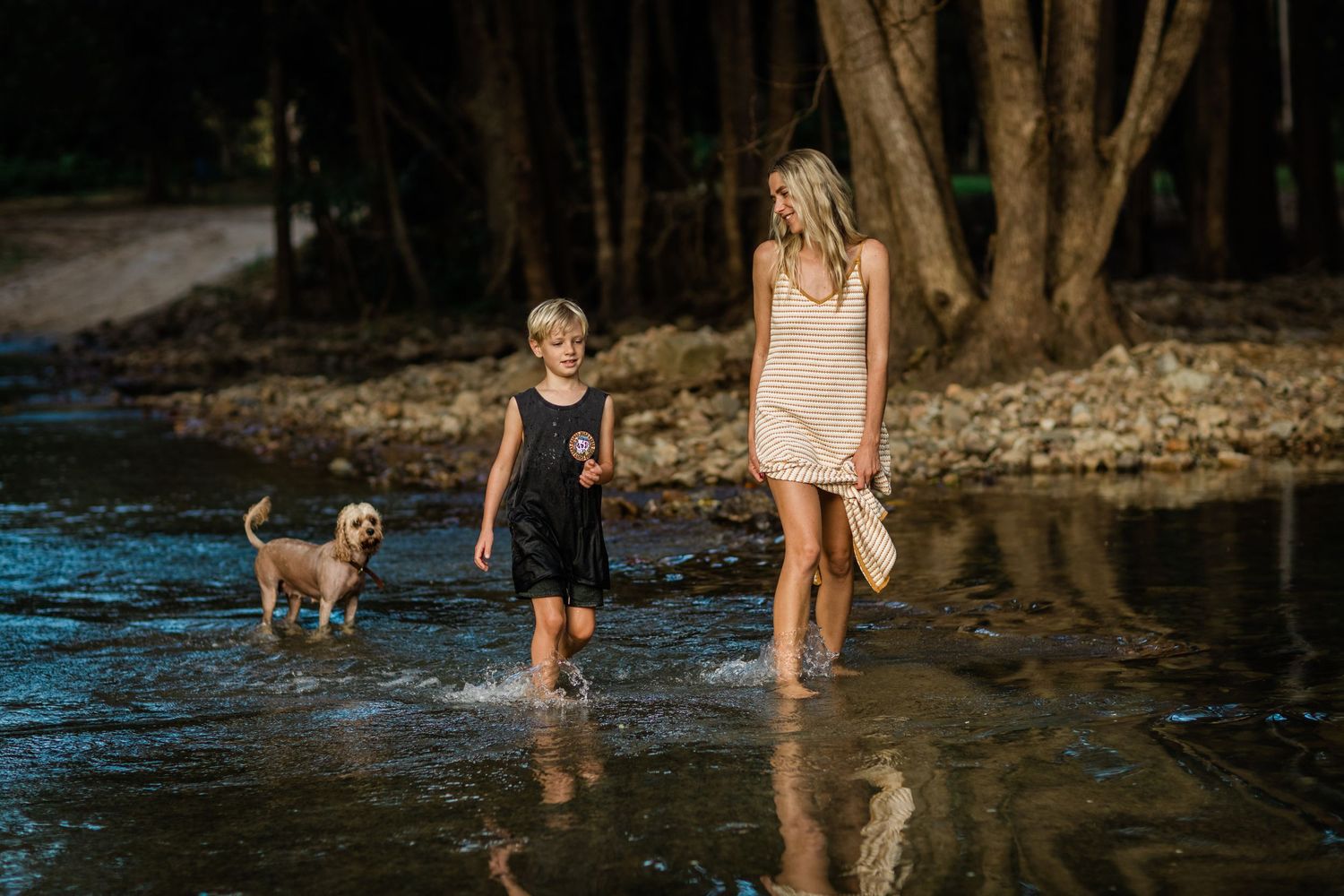 People exploring a shallow stream together near old trees.Gold Coast candid family photographer.