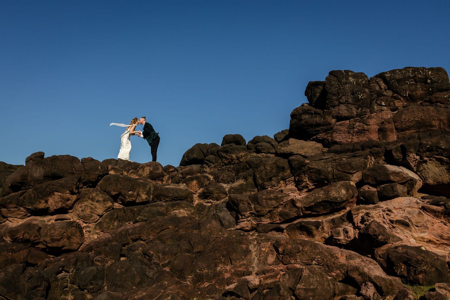 Silhouettes stand against deep blue sky on rugged red rock cliffs during sunset in desert landscape.
