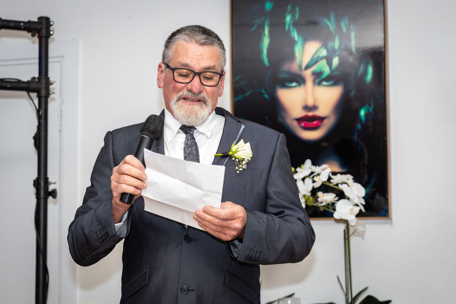 A person in a dark suit reads a letter while standing in front of colorful wall art.