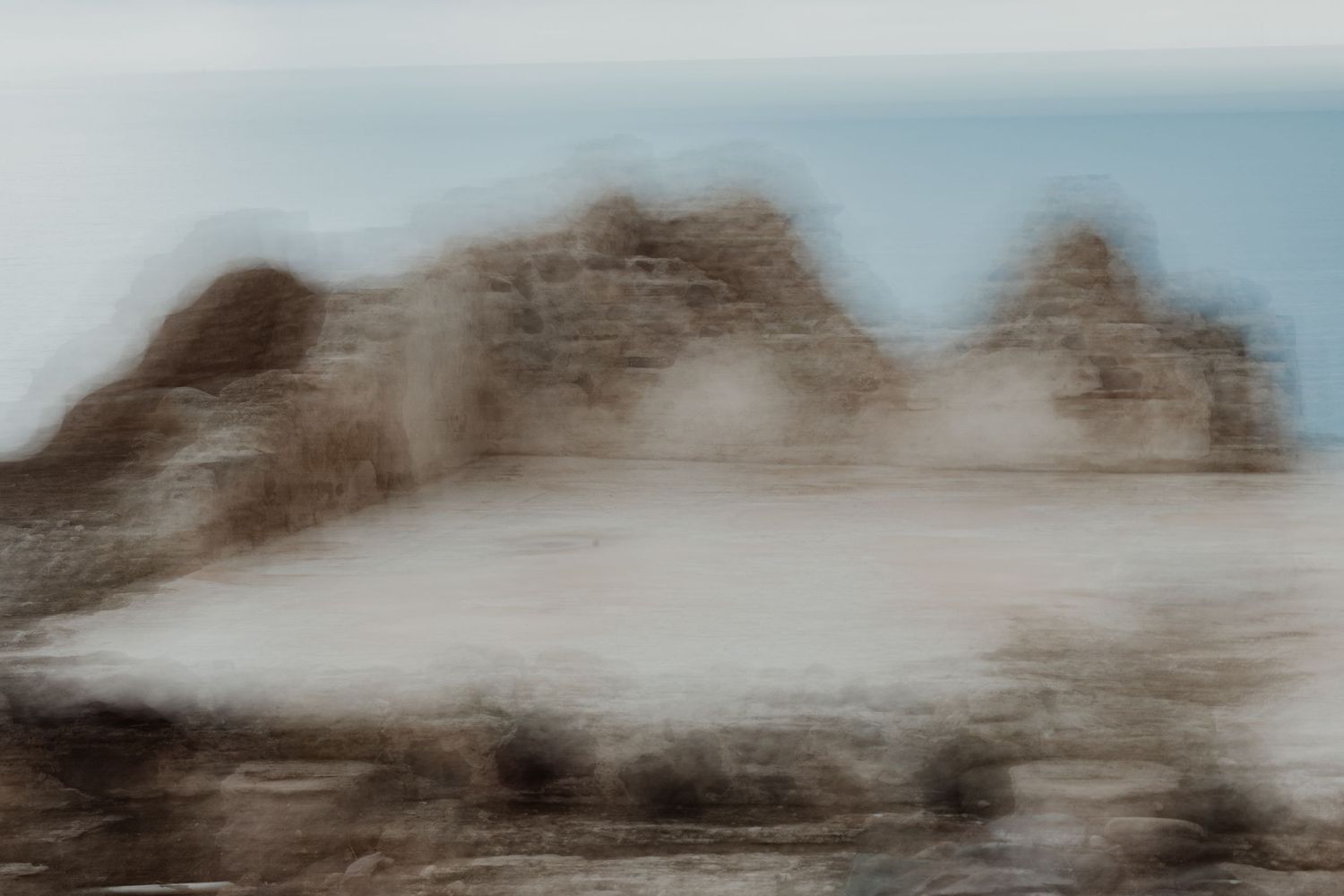 Blurred mountain landscape with misty peaks against pale blue sky.