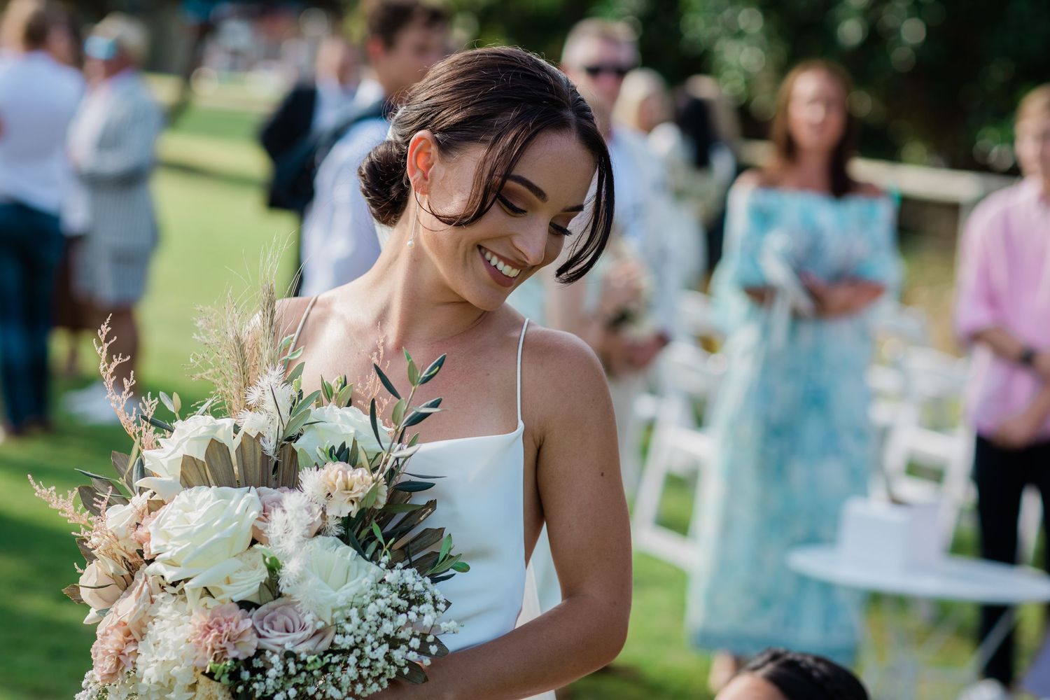 Wedding guests seated on white chairs during outdoor garden ceremony.