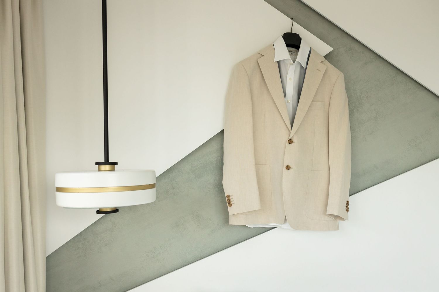 Beige suit jacket hanging on wall with modern pendant light fixture.