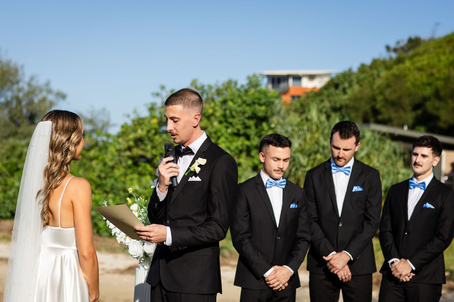 Wedding party lined up outdoors with groomsmen in black tuxedos.beach wedding currumbin surf club wedding