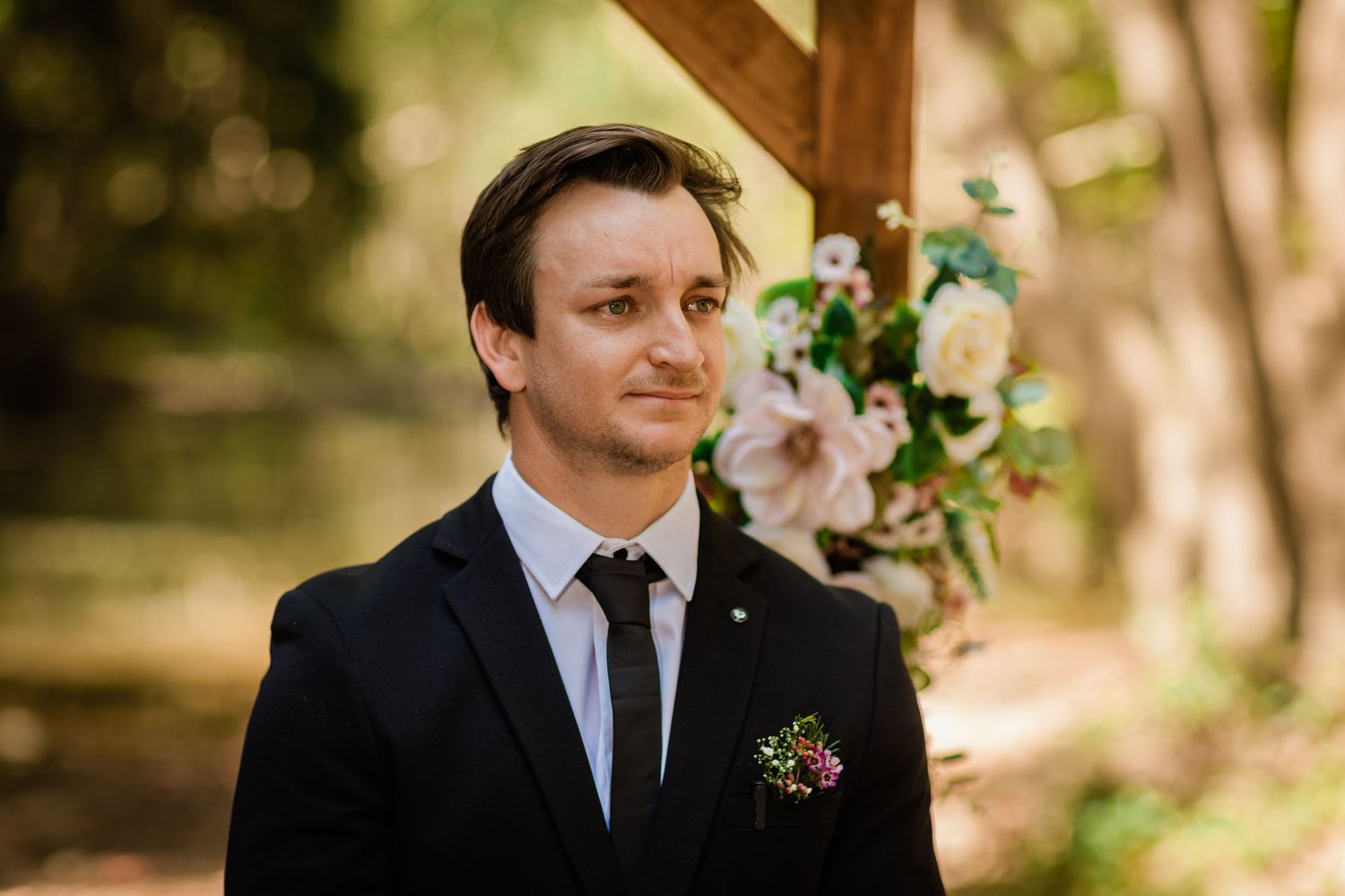 Couple exchanges vows beneath a wooden arbor adorned with greenery in a forest setting.Currumbin Valley wedding photography Gold Coast