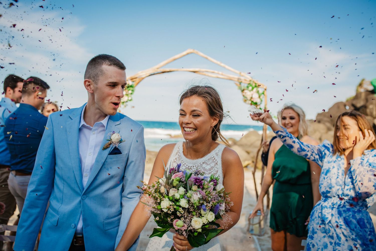 Wedding celebration with confetti and guests gathered under blue skies by the ocean.Gold Coast beach wedding photography. Froggies beach