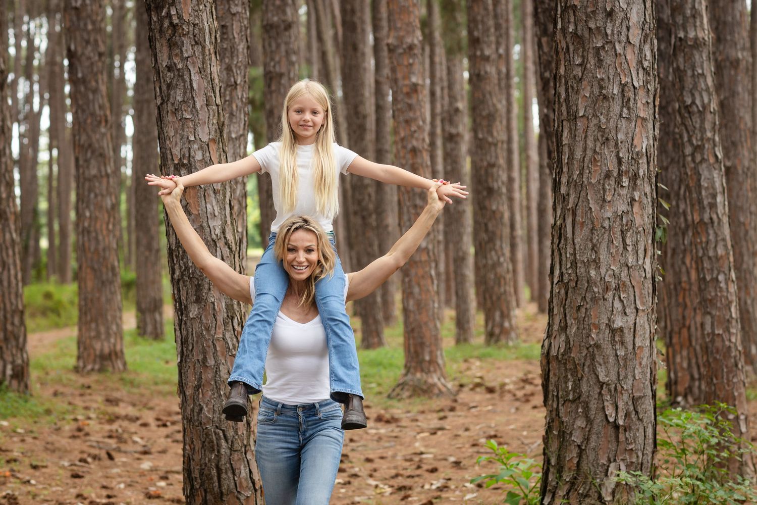 Two people share joyful moments while walking through a serene pine forest path.