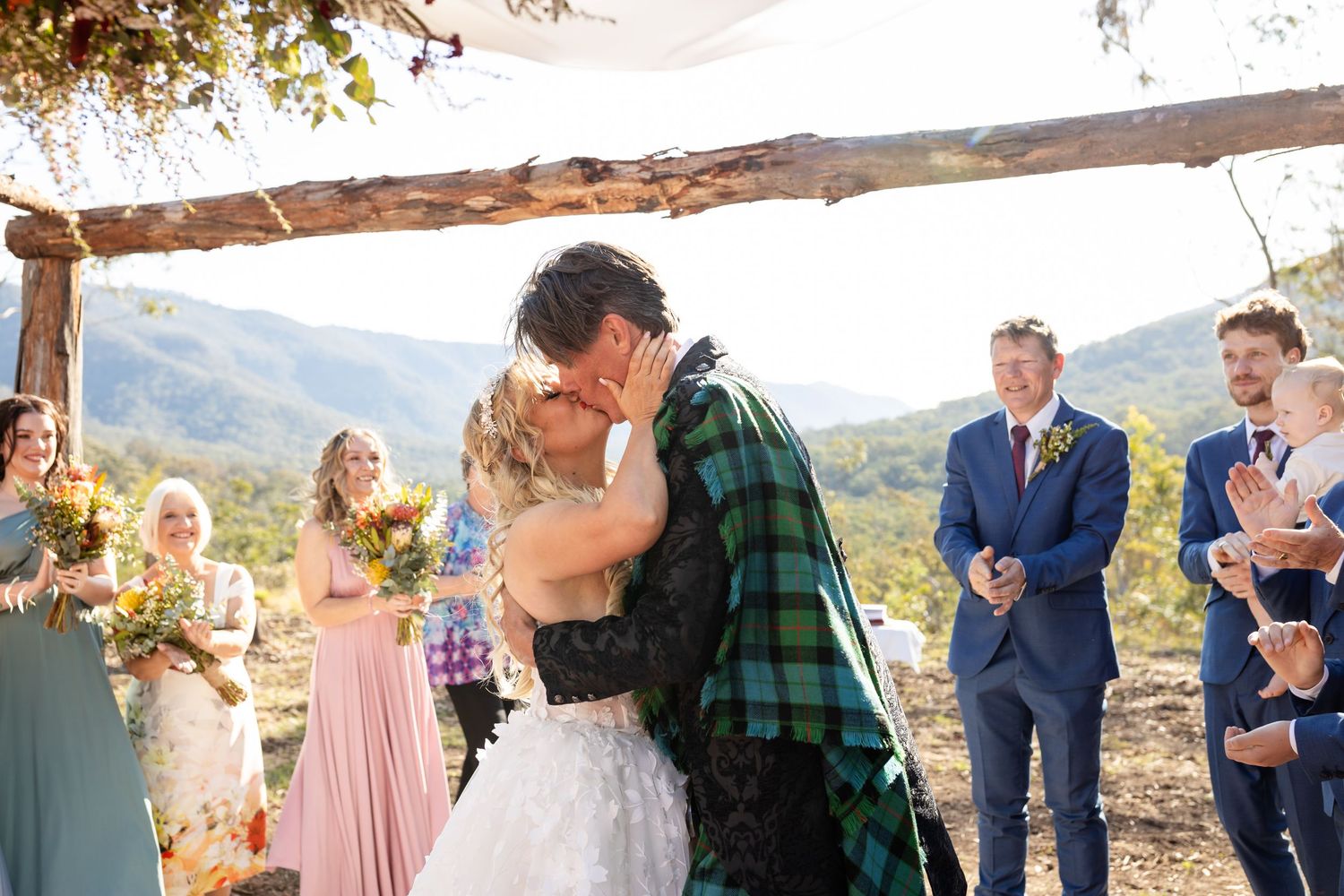 Wedding party celebrates outdoors with mountains and trees in the background during sunset ceremony.Gold Coast wedding photographer