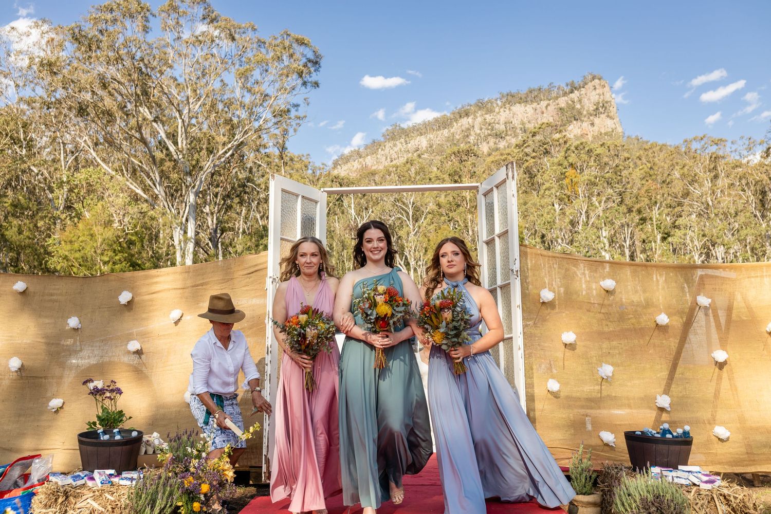 Wedding party standing in front of a decorated rustic wooden arch with mountain views.