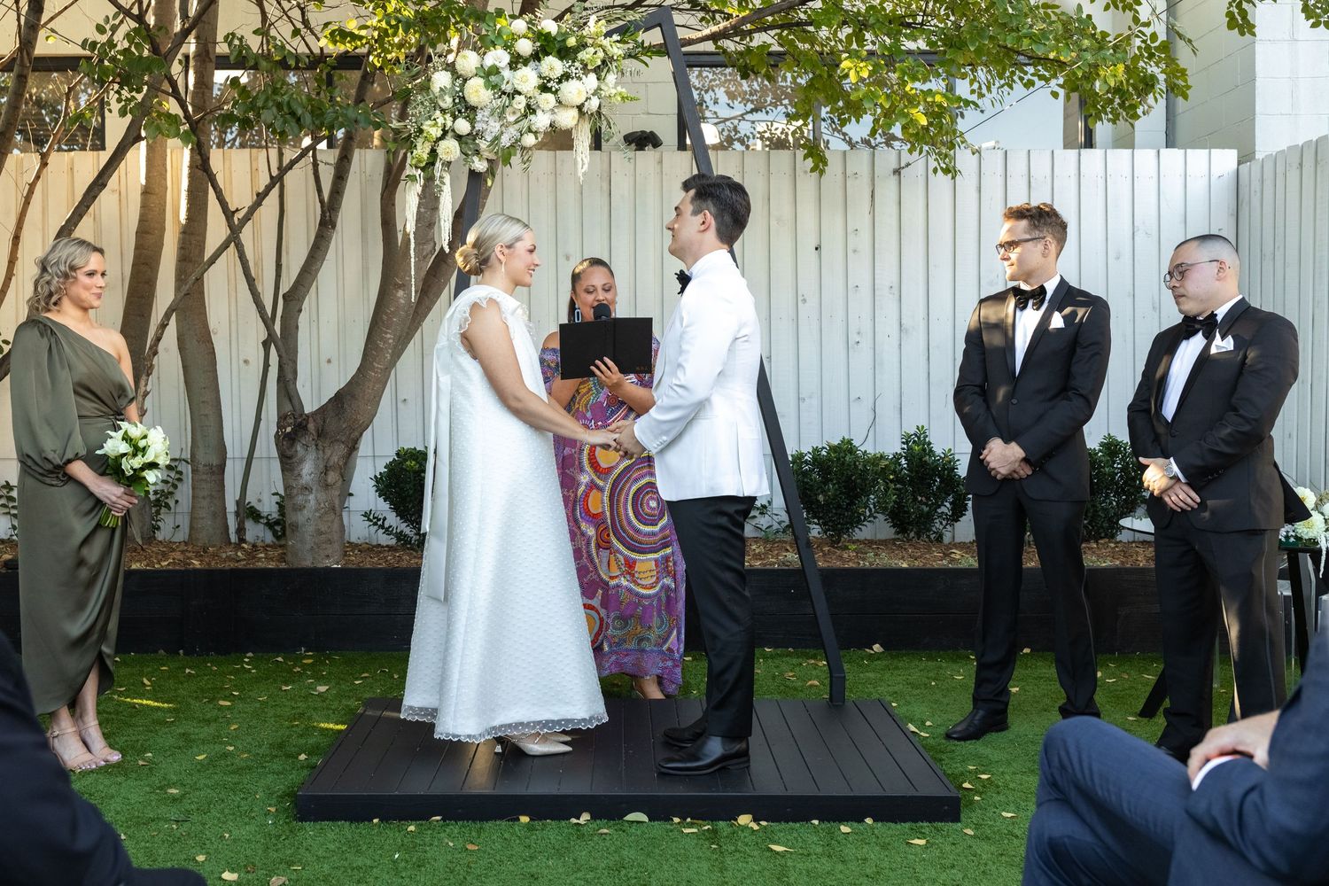 Garden wedding ceremony setup with white fence and green foliage.