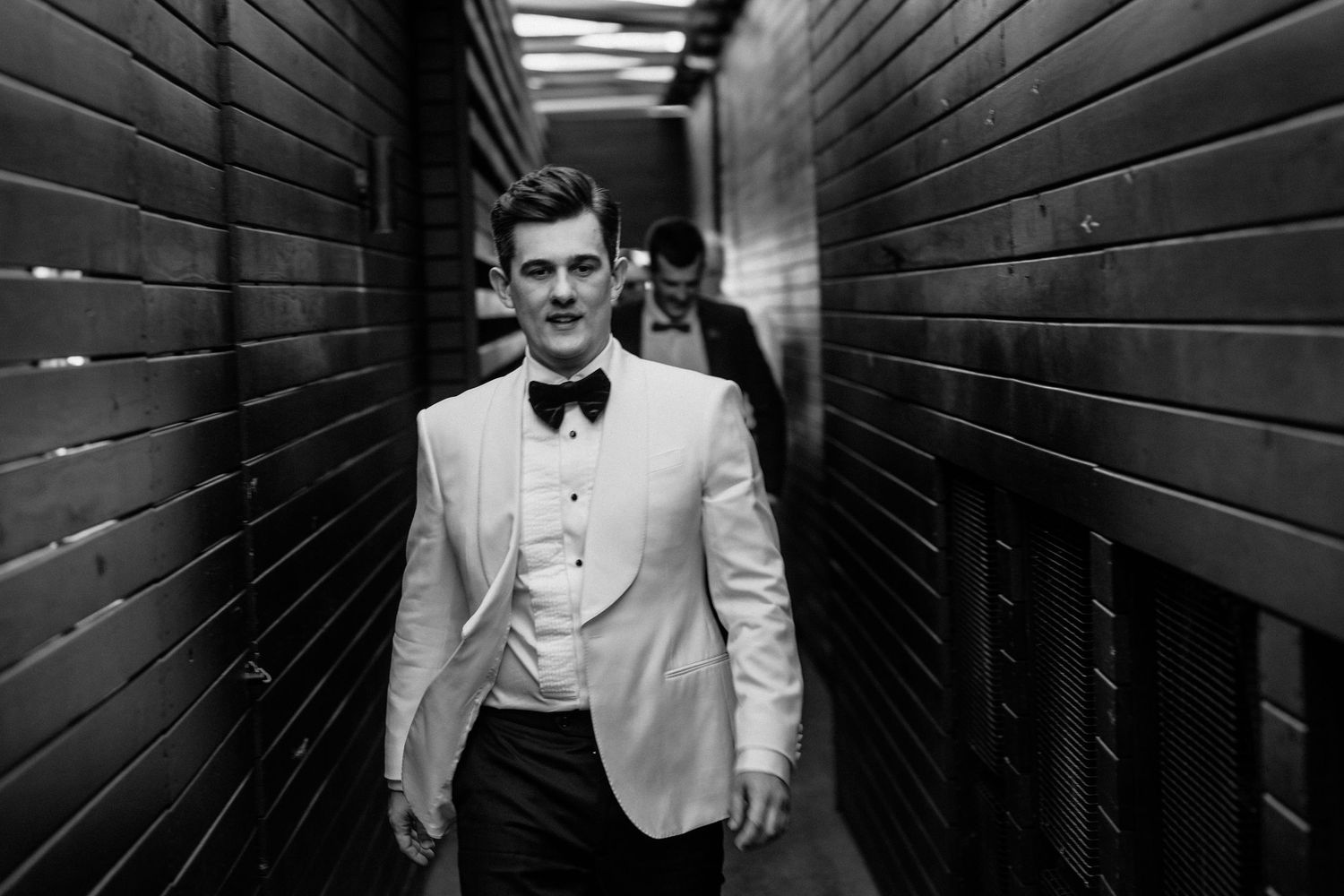 Wedding party members walking through modern hallway with dramatic lighting.
