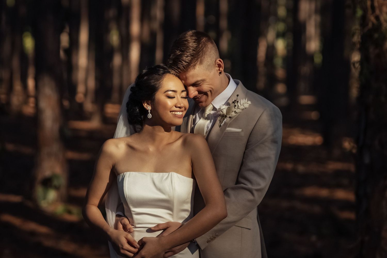 An intimate wedding portrait captured in a wooded forest setting with warm lighting.