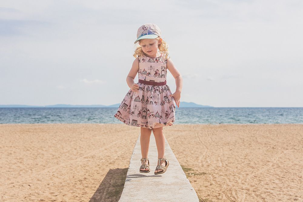 Young girl in a floral dress and headband poses on a beach boardwalk with ocean in the background.