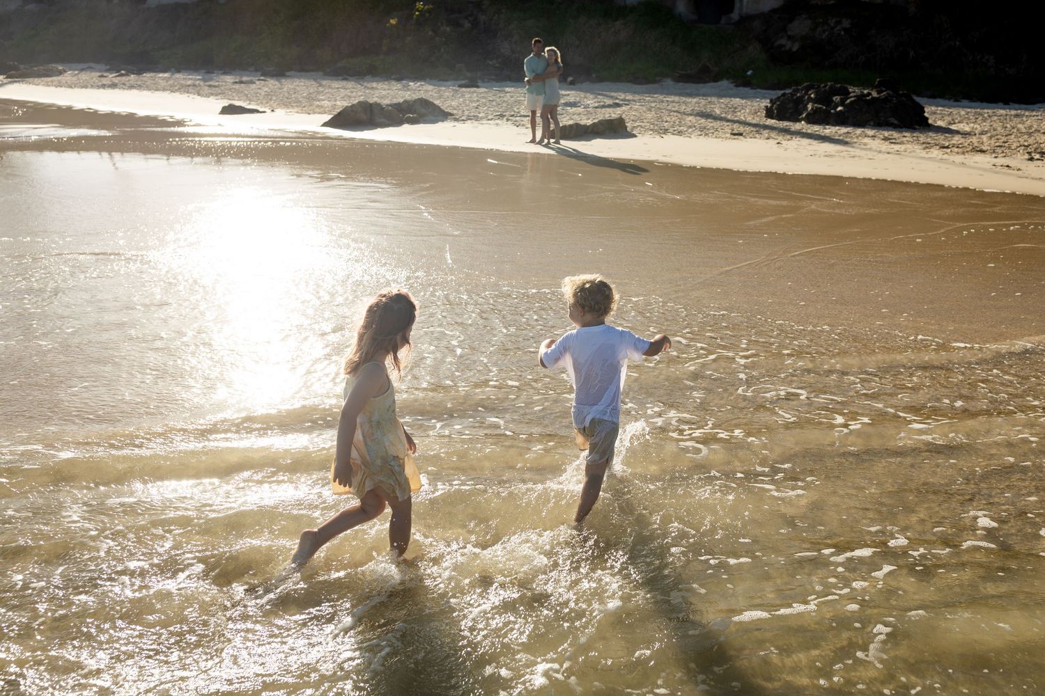 People playing in shallow ocean waves during golden sunset.Family photography Kirra beach Gold Coast.Gold Coast candid family photographer.