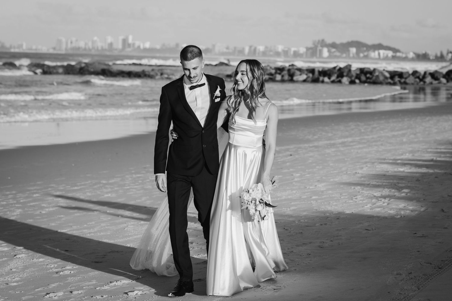 Couple walking along beach shoreline in formal wedding attire.beach wedding currumbin surf club wedding
