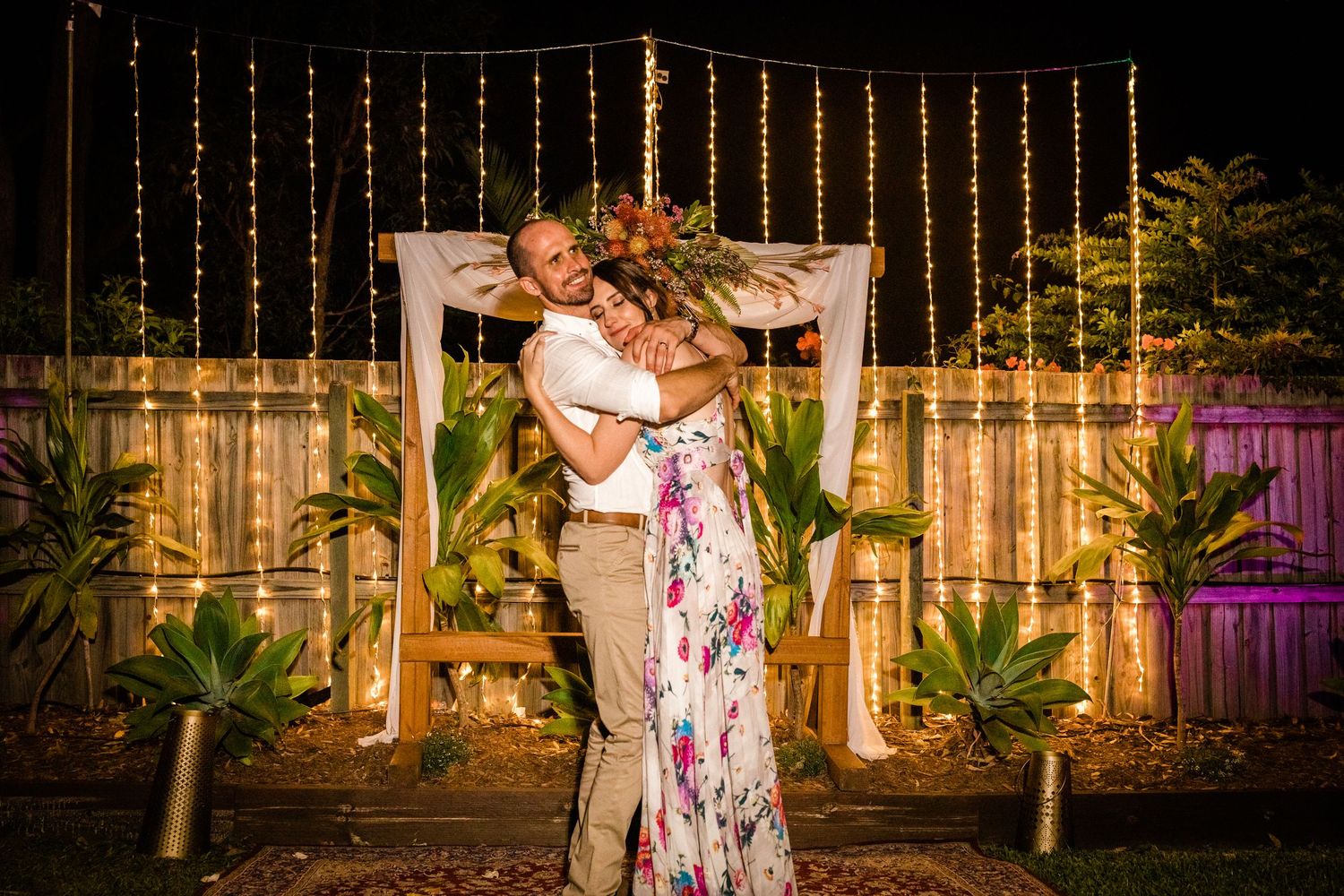 String lights illuminate an outdoor evening party space with palm trees.
