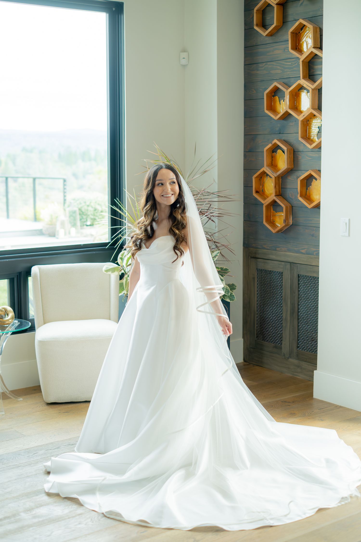 Bride in elegant white strapless ball gown with veil posing in bright modern venue with honeycomb wall decor.