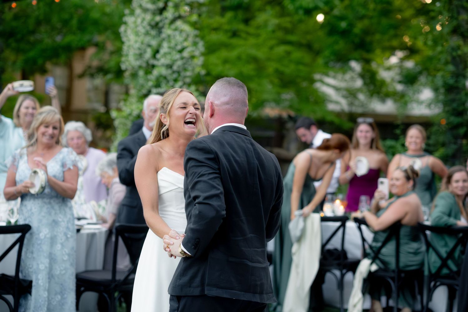 Laughing bride and groom sharing their first dance at an outdoor evening wedding reception.