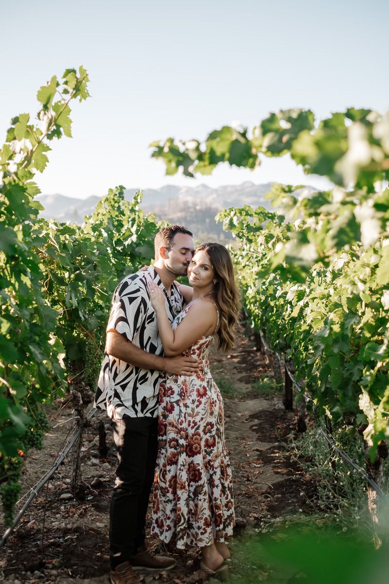 Couple embracing romantically between rows of grapevines in a sunlit vineyard.