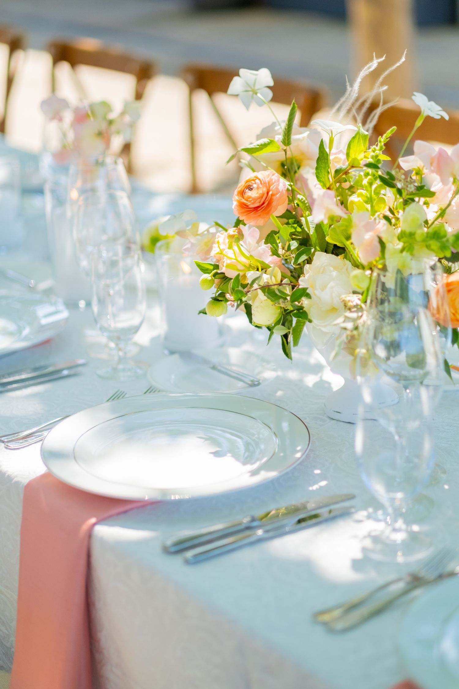 Close-up of elegant wedding table setting with peach roses, glass chargers and pink napkins.