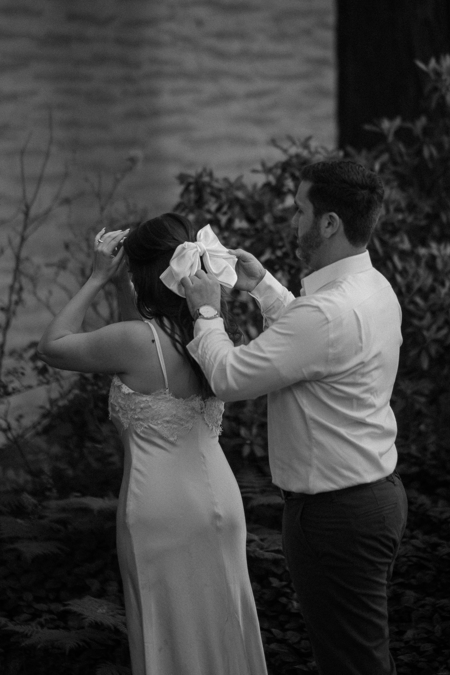 Groom tying a white bow in brides hair during an outdoor engagement photo session.