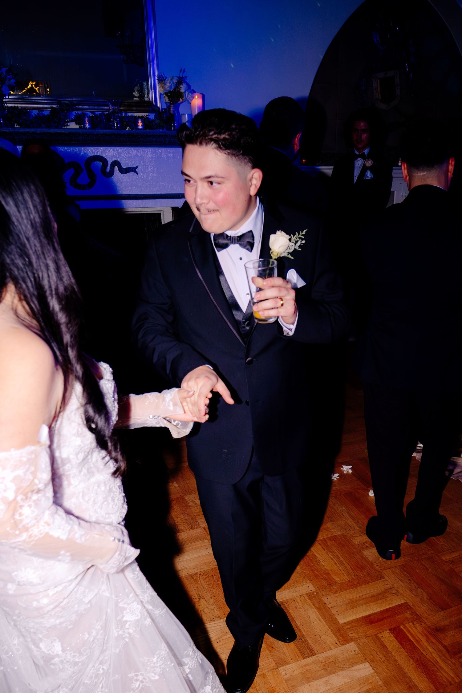Groom in black tuxedo with boutonniere dancing with bride in white lace gown at elegant wedding reception.
