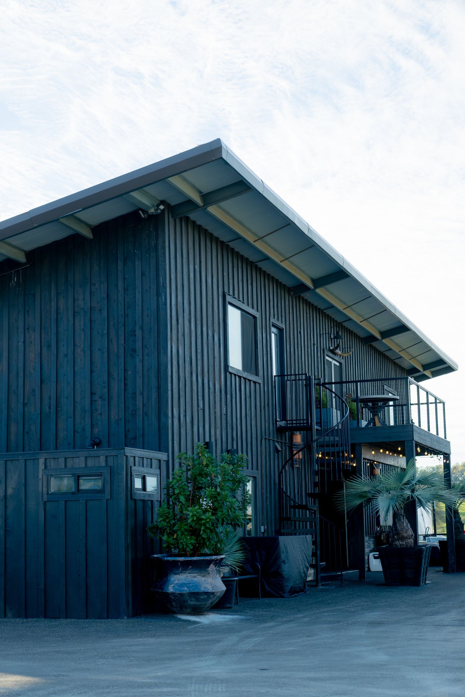 Dark navy barn-style wedding venue exterior with spiral staircase and string lights at dusk.