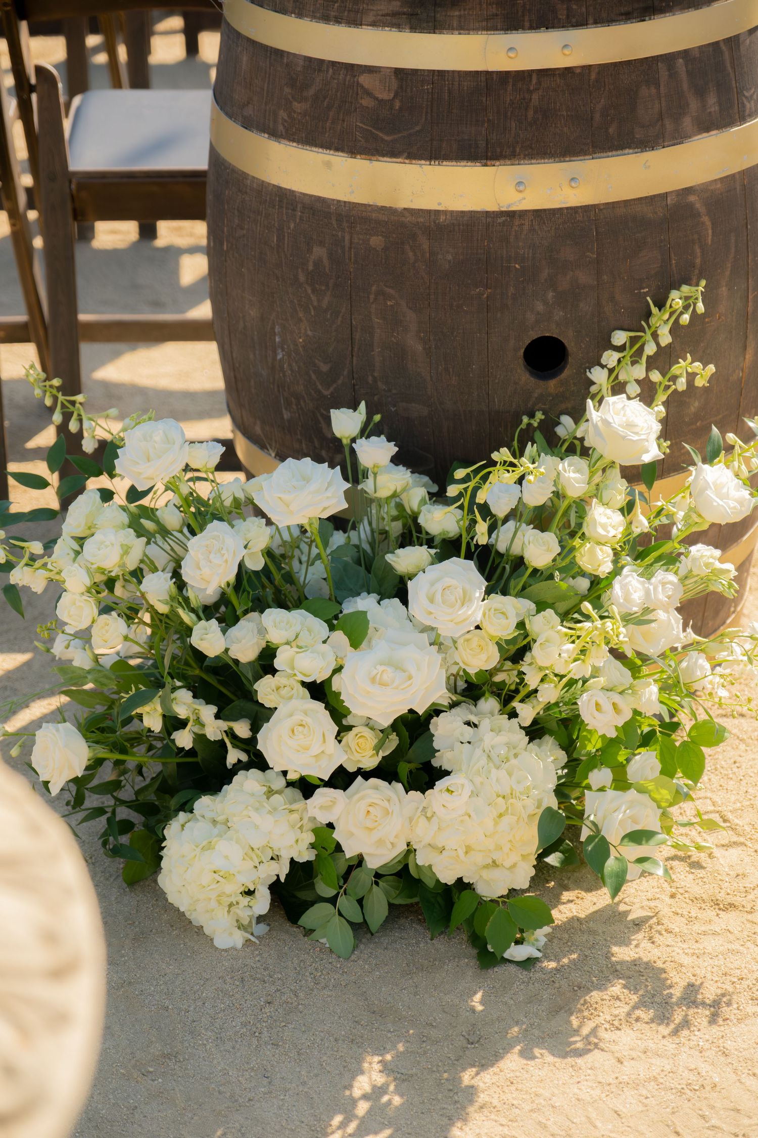 Lush arrangement of white roses and hydrangeas placed beside rustic wooden wine barrel at ceremony.
