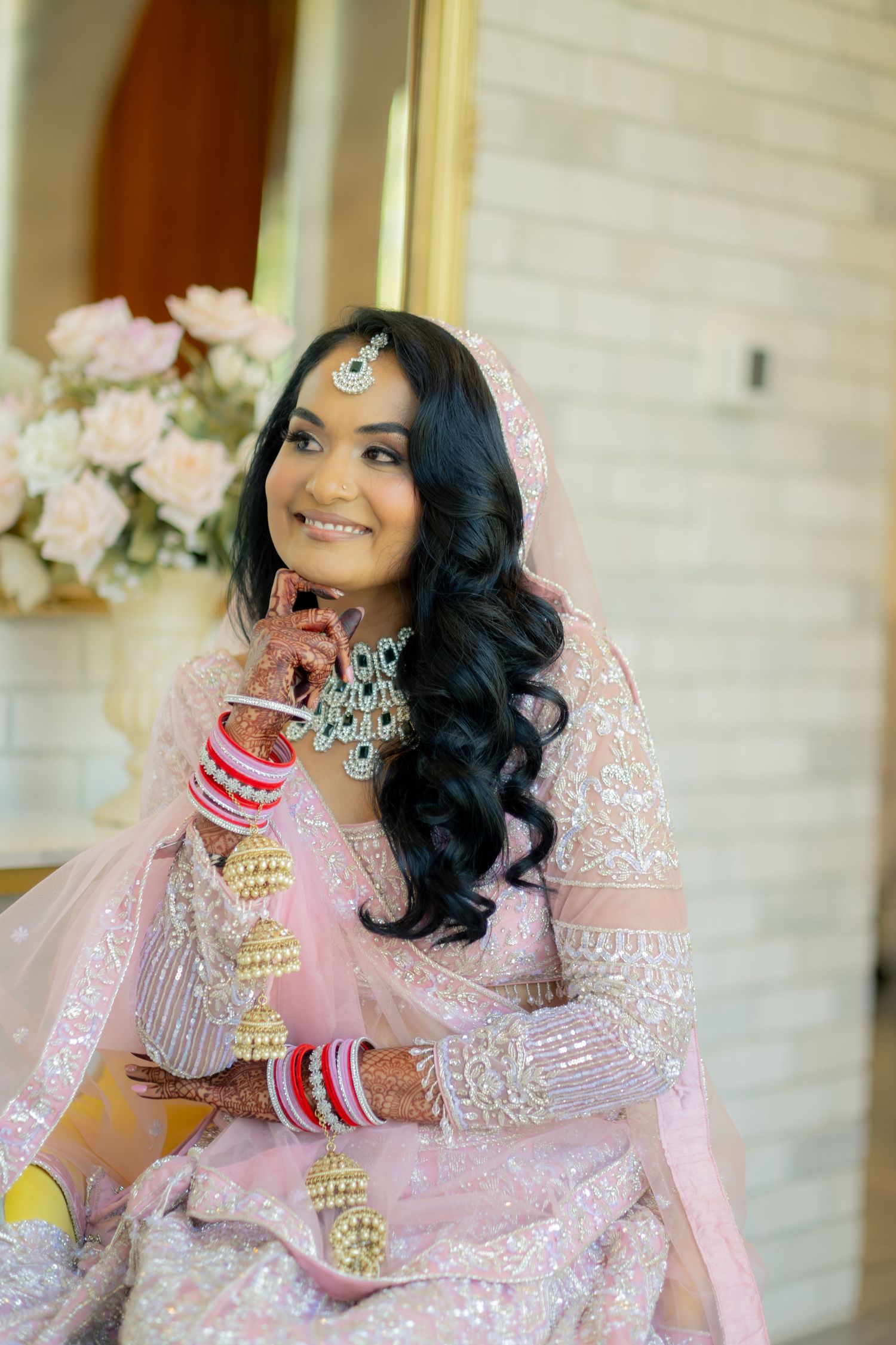 Beautiful Indian bride in pink lehenga with mehndi and traditional jewelry smiles gracefully.