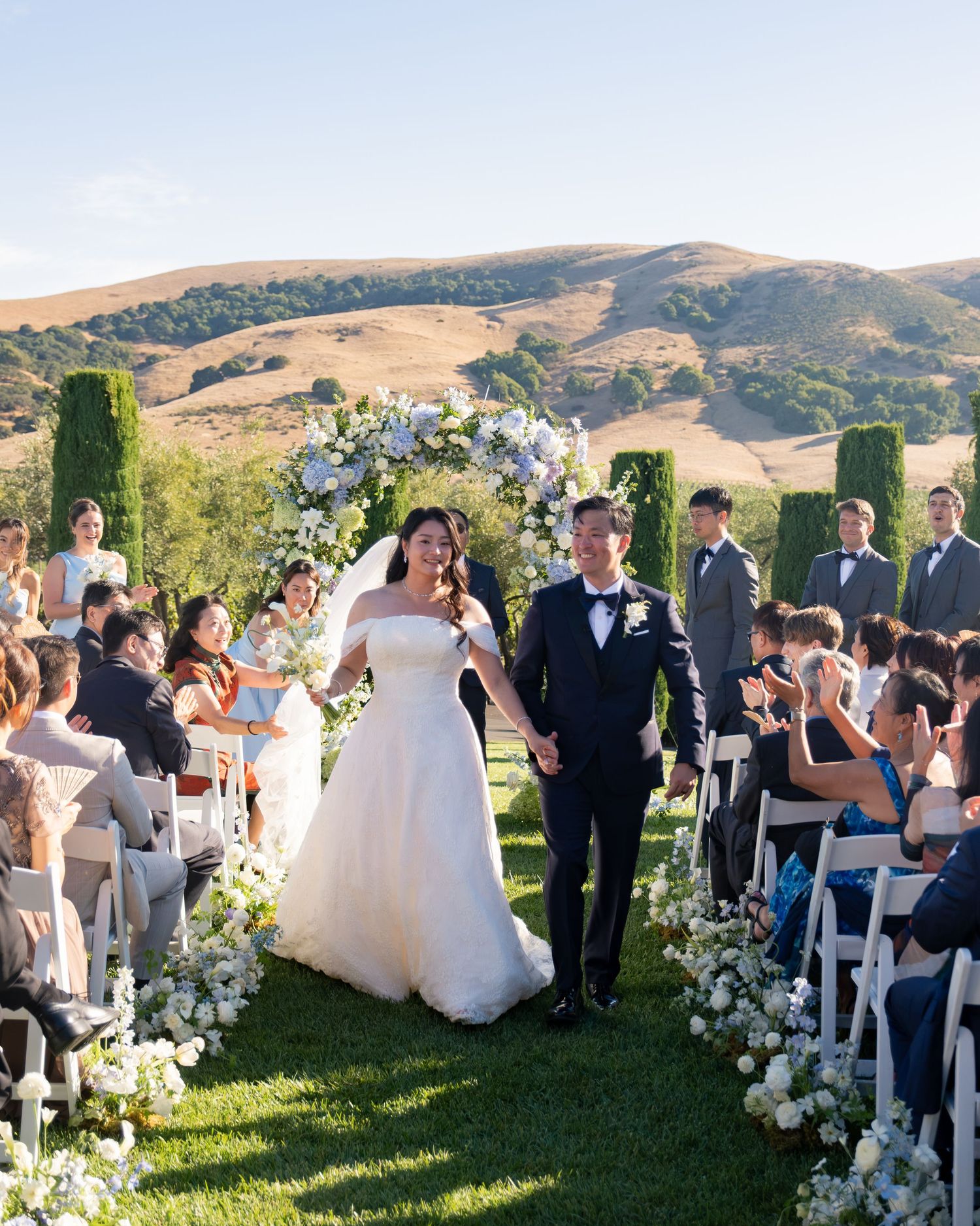 Bride and groom walk back down aisle after ceremony with golden California hills in background.