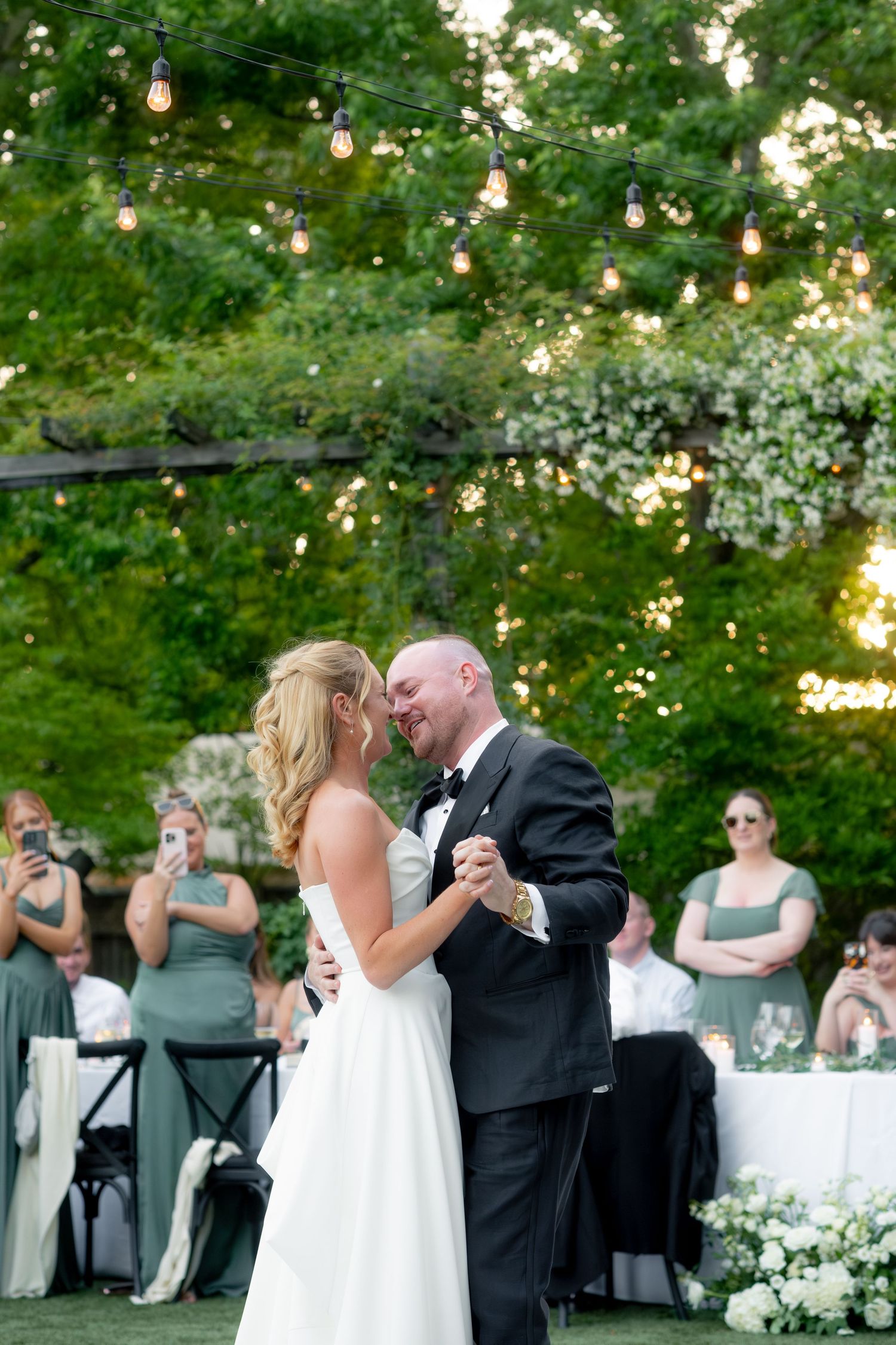 Bride and groom sharing their first dance under warm string lights at an outdoor wedding reception.