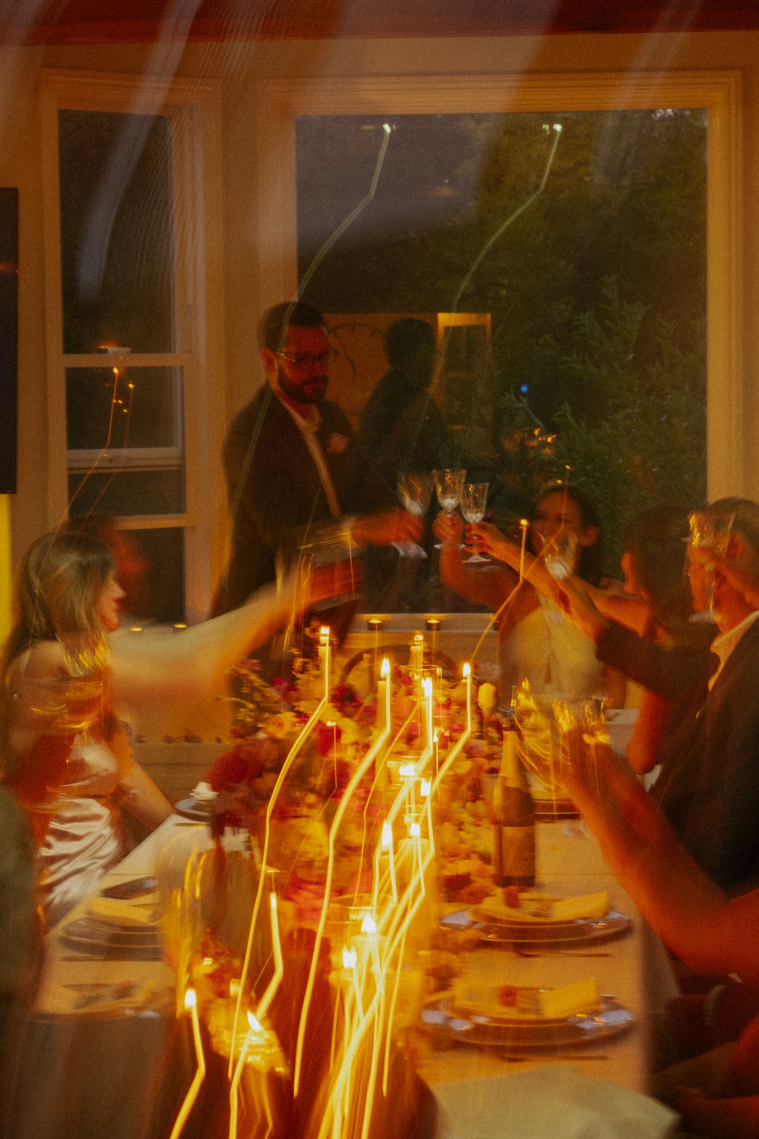 Wedding guests raise glasses in a candlelit toast around a beautifully decorated dinner table during an intimate reception.