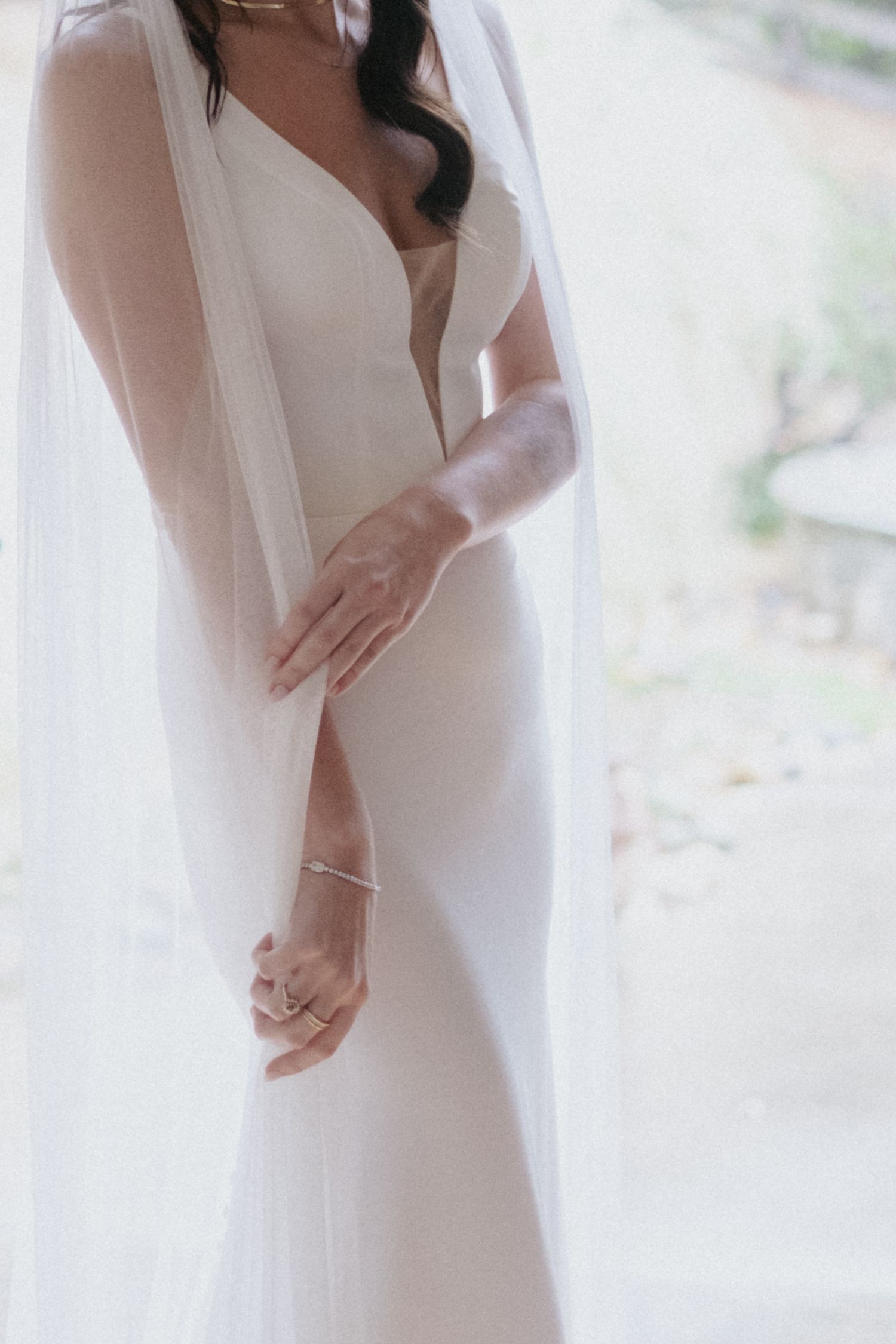 Elegant bride in a sleek white satin wedding gown with a flowing veil, showcasing delicate jewelry.