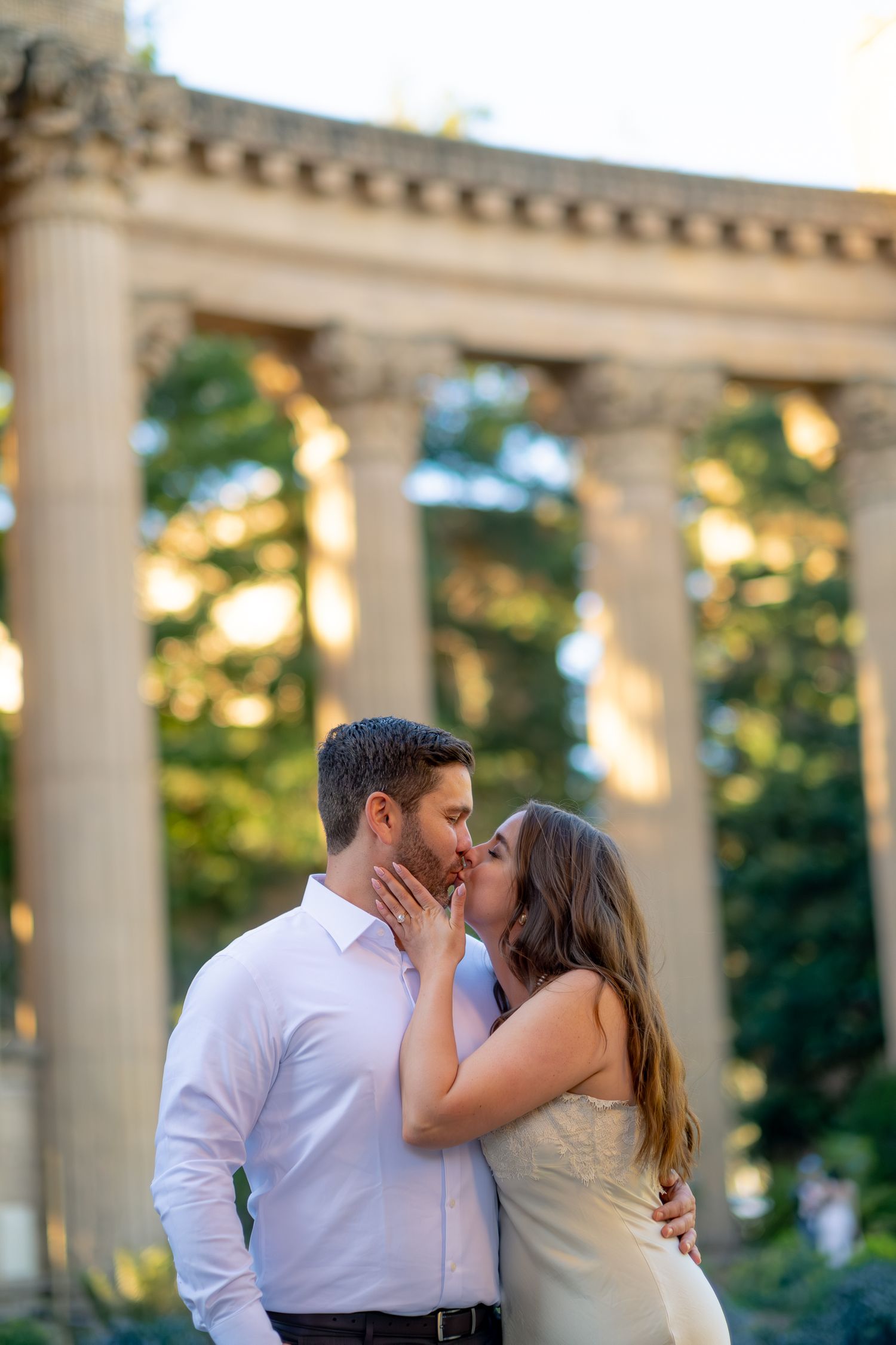 Couple sharing a romantic kiss in front of classical columns at the Palace of Fine Arts, San Francisco.