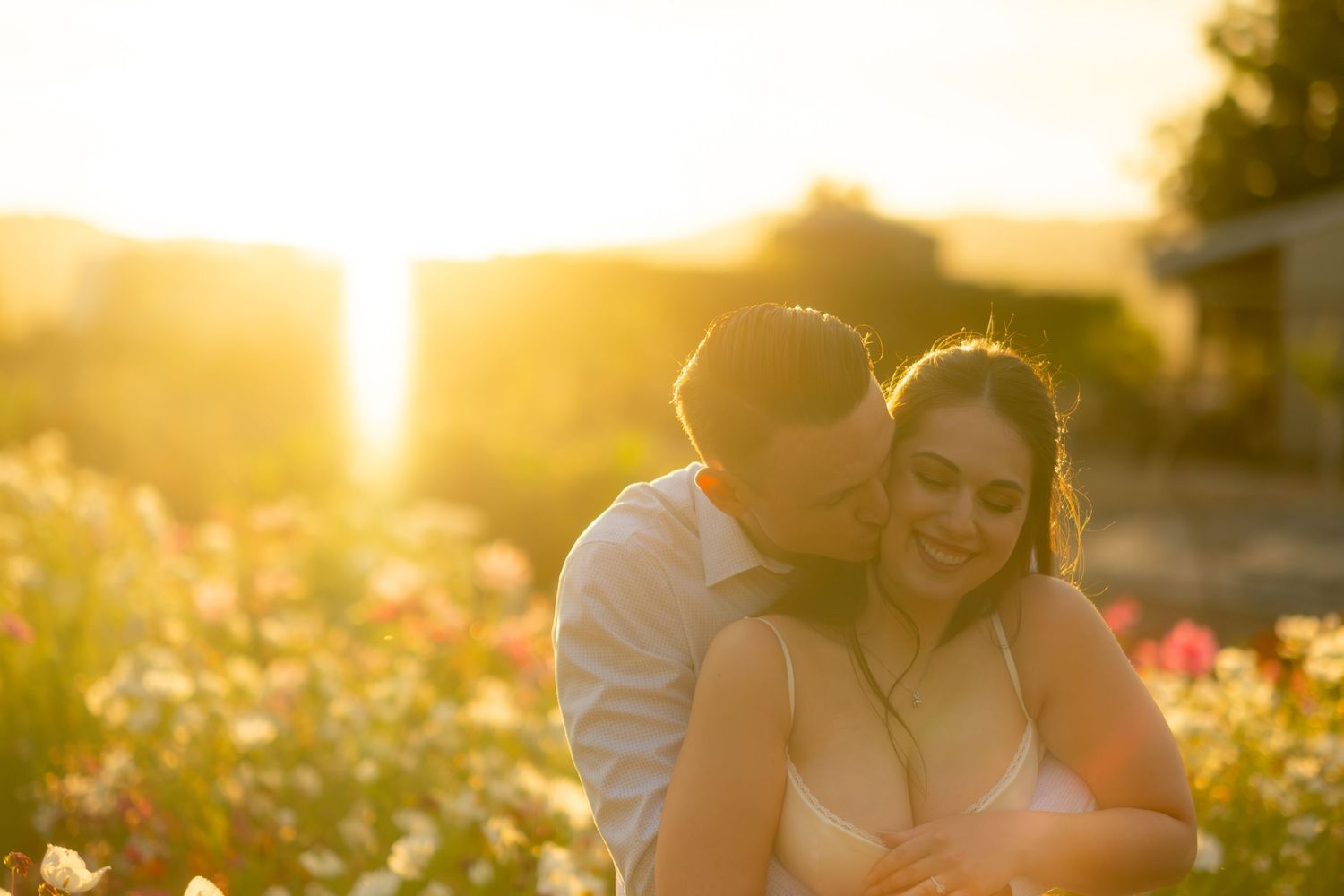 Groom kissing bride's cheek in a flower field during a glowing golden sunset.