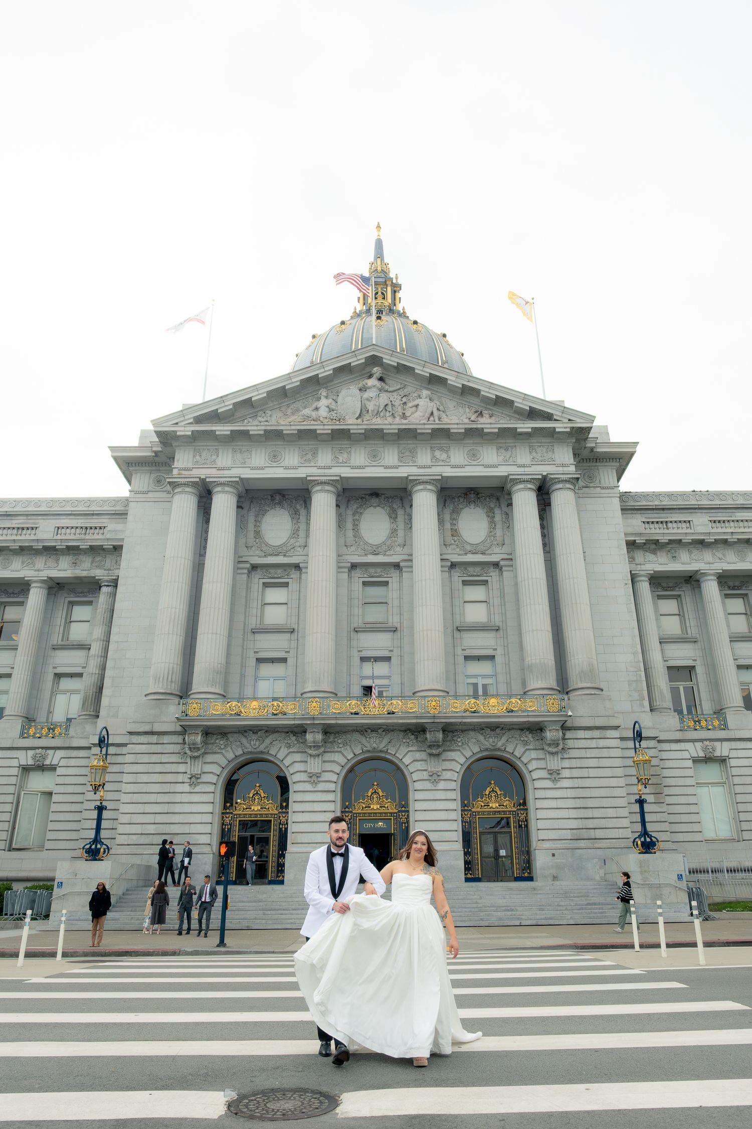 Bride and groom crossing street in front of San Francisco City Hall in wedding attire on their wedding day.