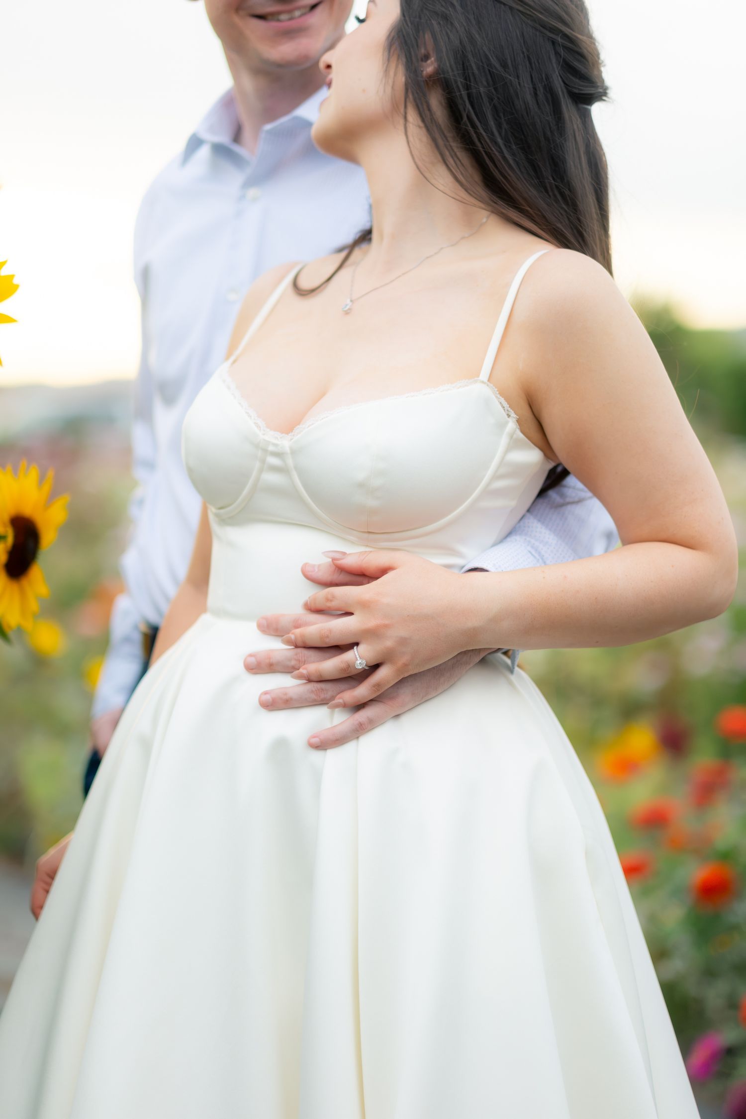 Couple embracing in colorful garden with sunflowers, woman in white dress.