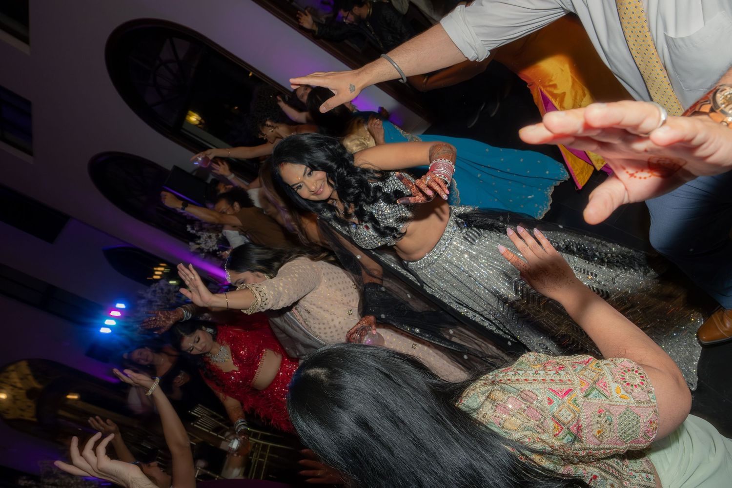Guests in colorful traditional Indian attire dancing at a vibrant wedding reception party.