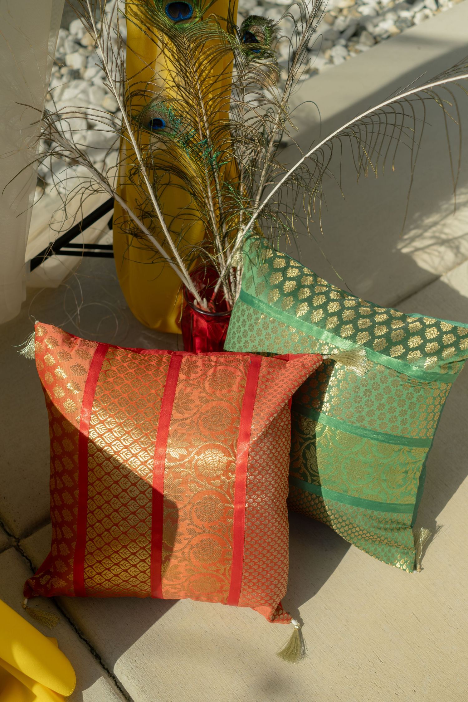 Colorful Indian silk brocade cushions with gold embroidery and peacock feathers displayed as wedding decor.