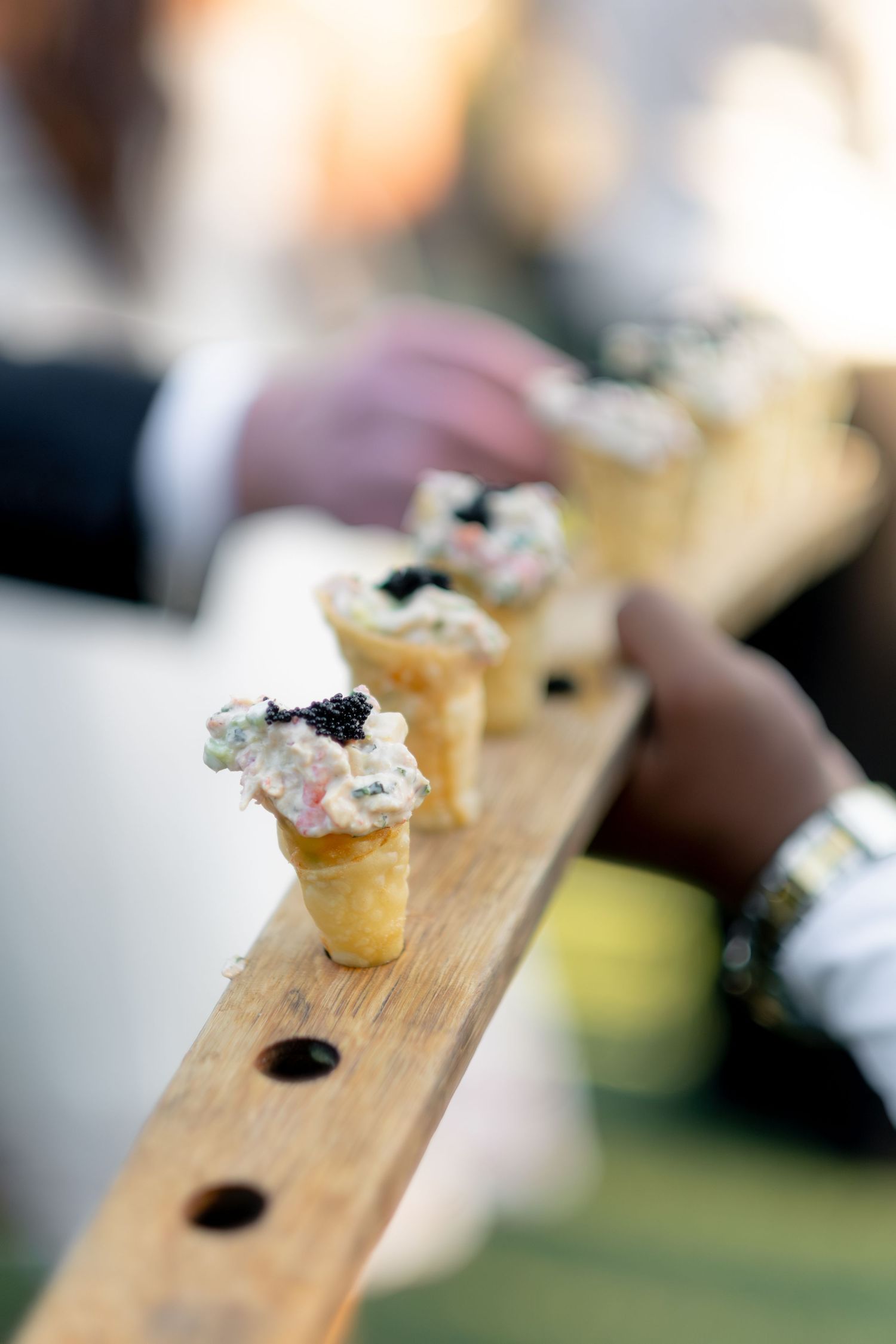 Elegant wedding appetizers in crispy cones topped with creamy filling and caviar displayed on a wooden serving board.