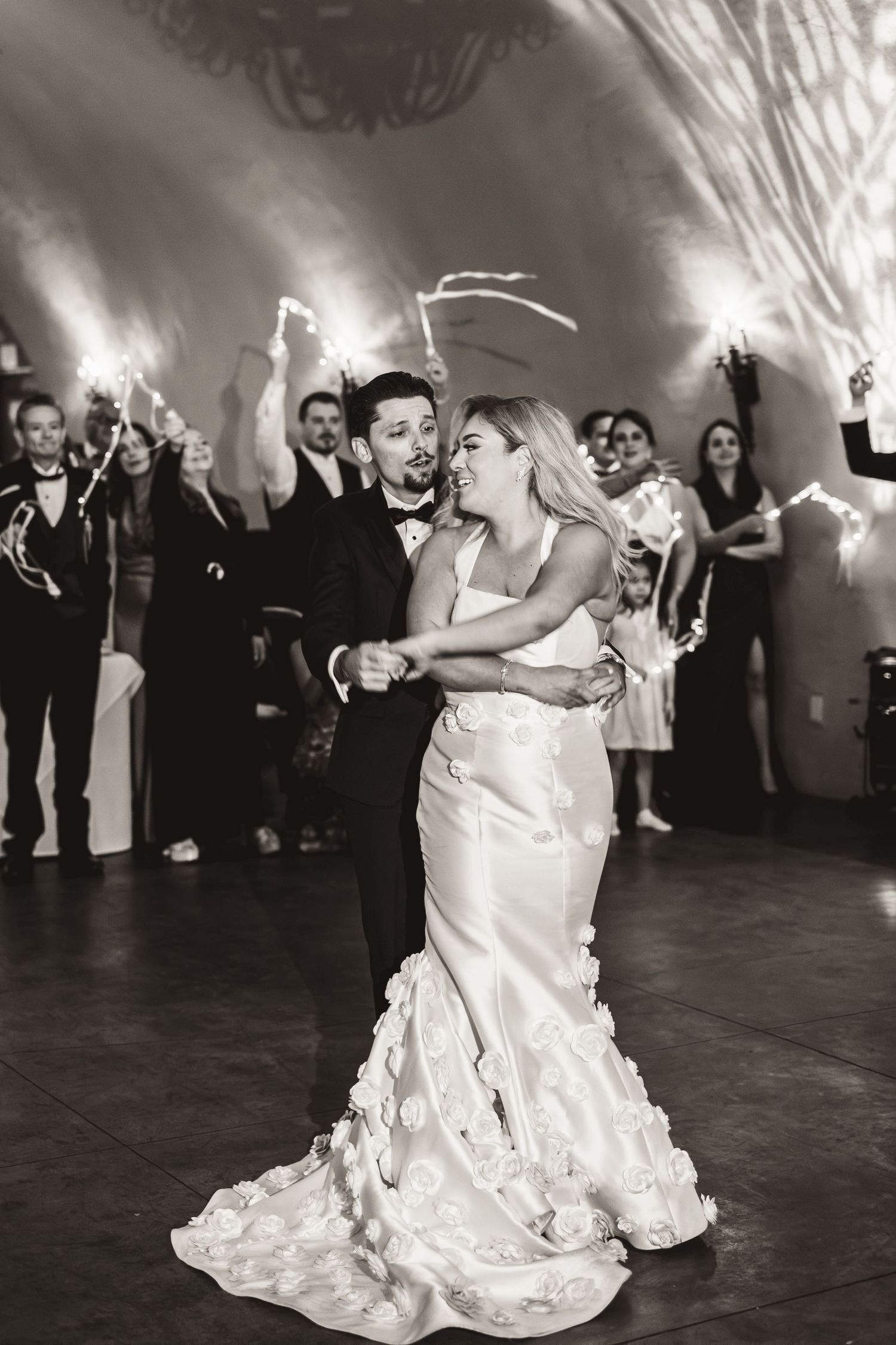 Black and white photo of bride and groom sharing first dance surrounded by sparkler-holding guests.