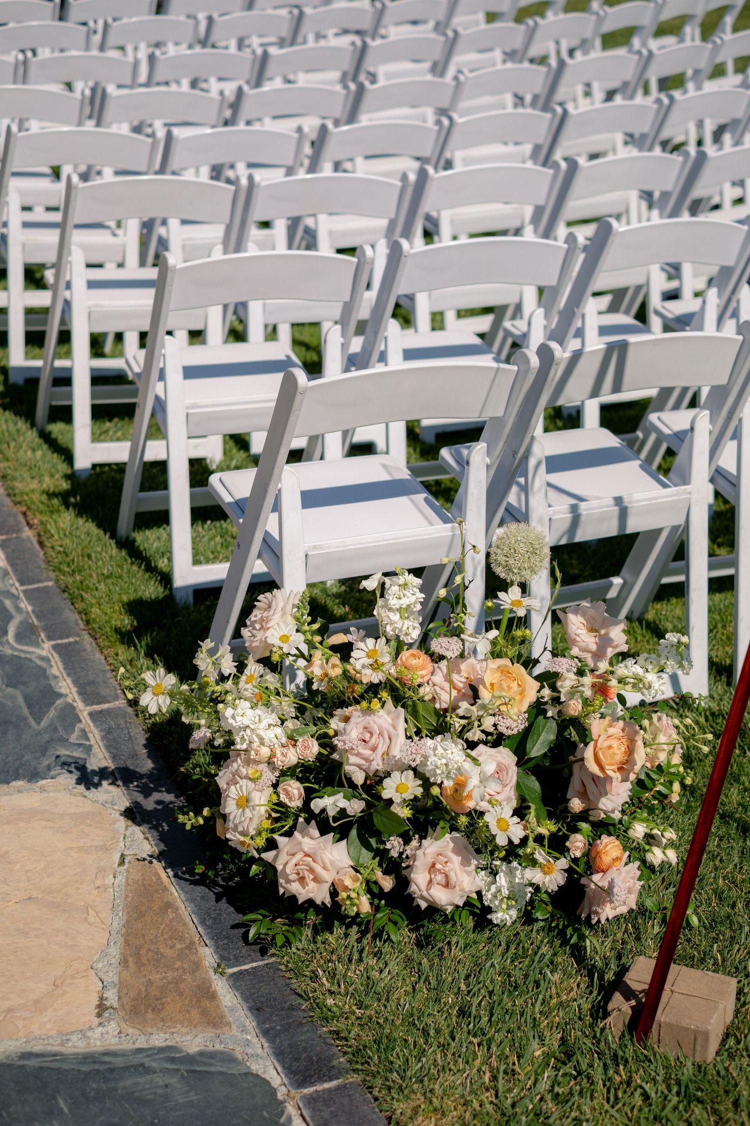 Rows of white folding chairs set up on grass with peach floral arrangements for ceremony.