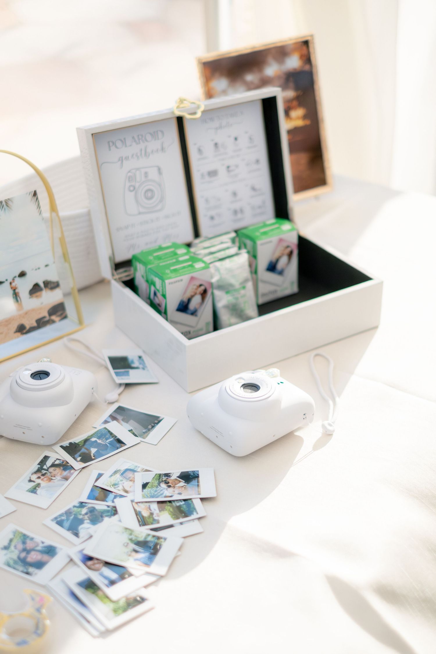 Polaroid guestbook station with Instax cameras, printed photos, and film packs in a white box at a wedding reception.