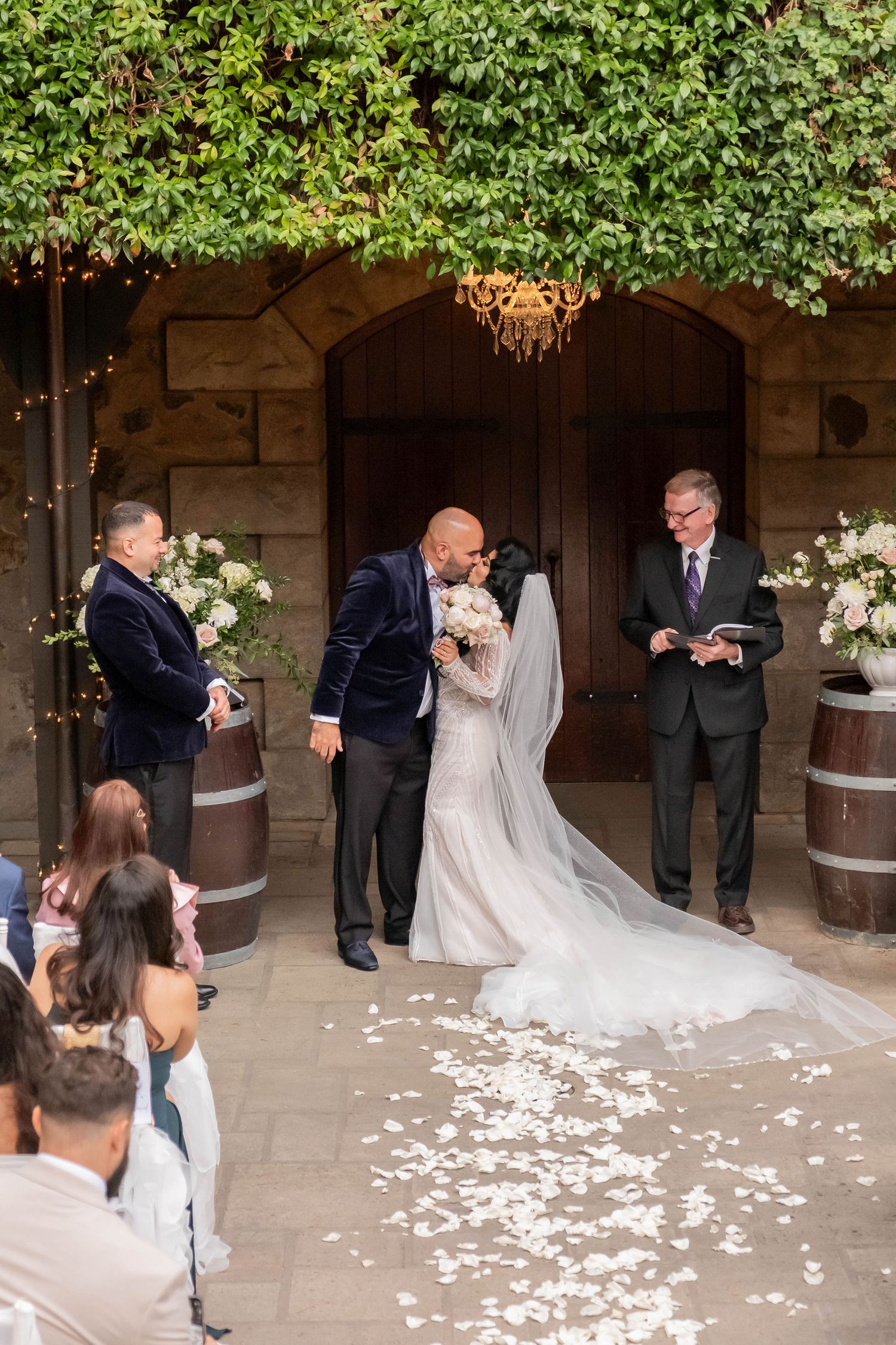 Bride and groom share their first kiss at the altar surrounded by floral arrangements and barrel decor.