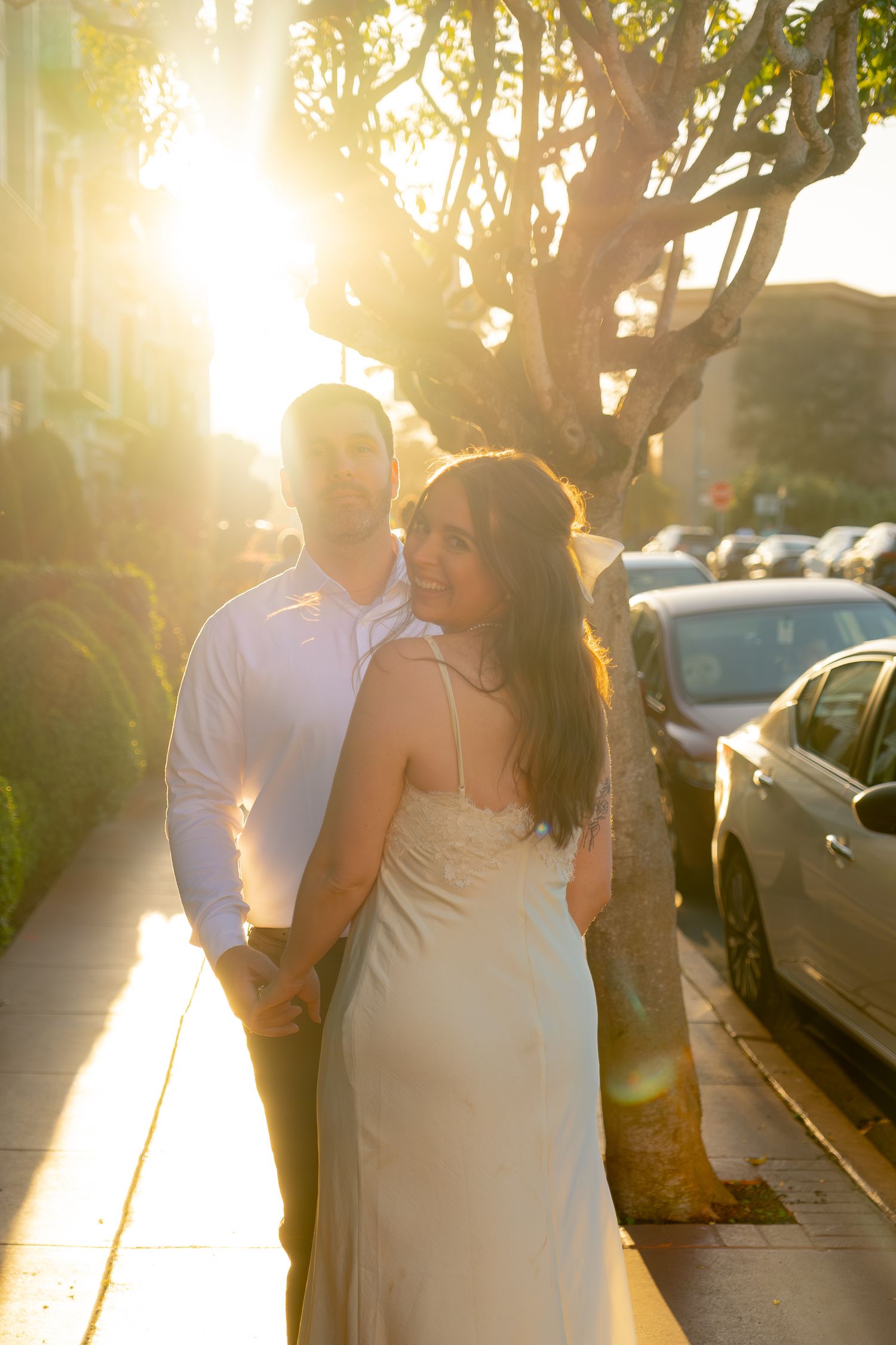 Couple walking hand in hand on a sun-drenched sidewalk during golden hour engagement session.