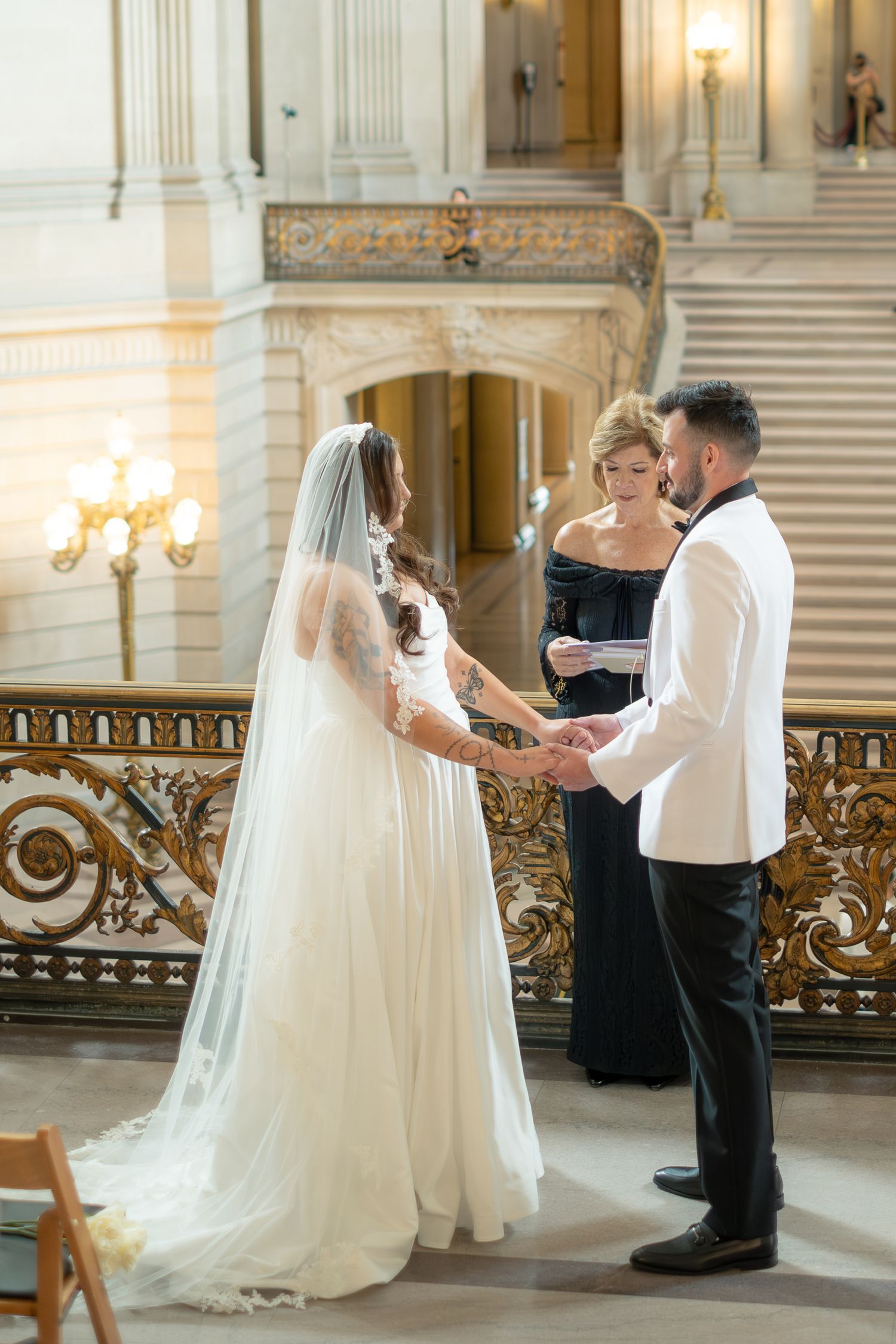 Bride and groom exchange vows at San Francisco City Hall with officiant in elegant black gown.