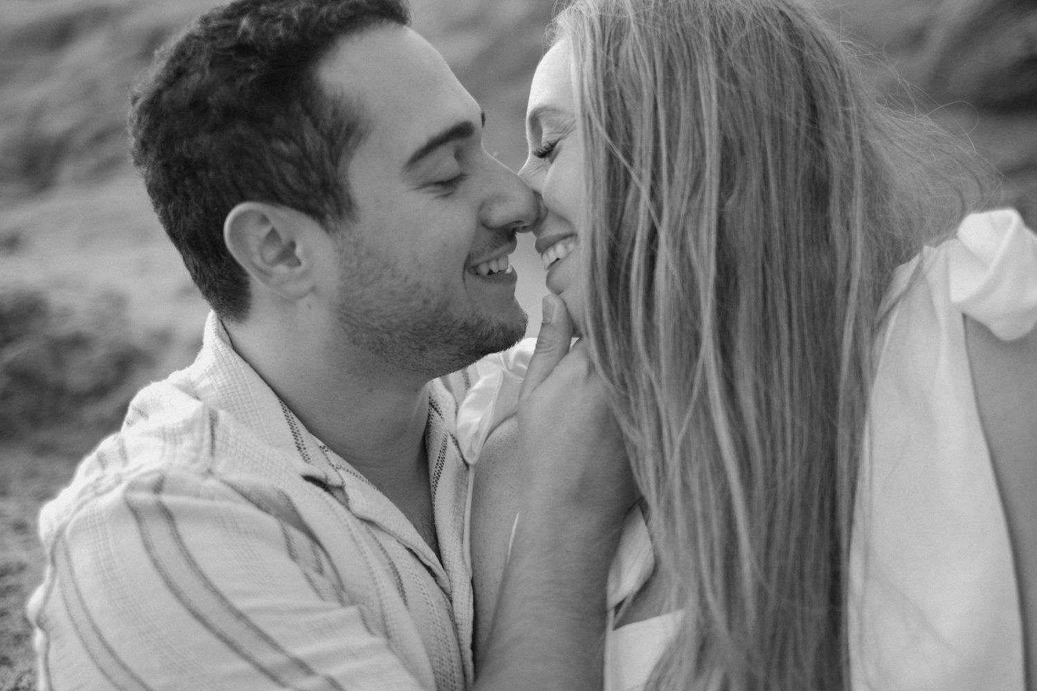 Black and white photo of smiling couple sharing a tender romantic moment outdoors.