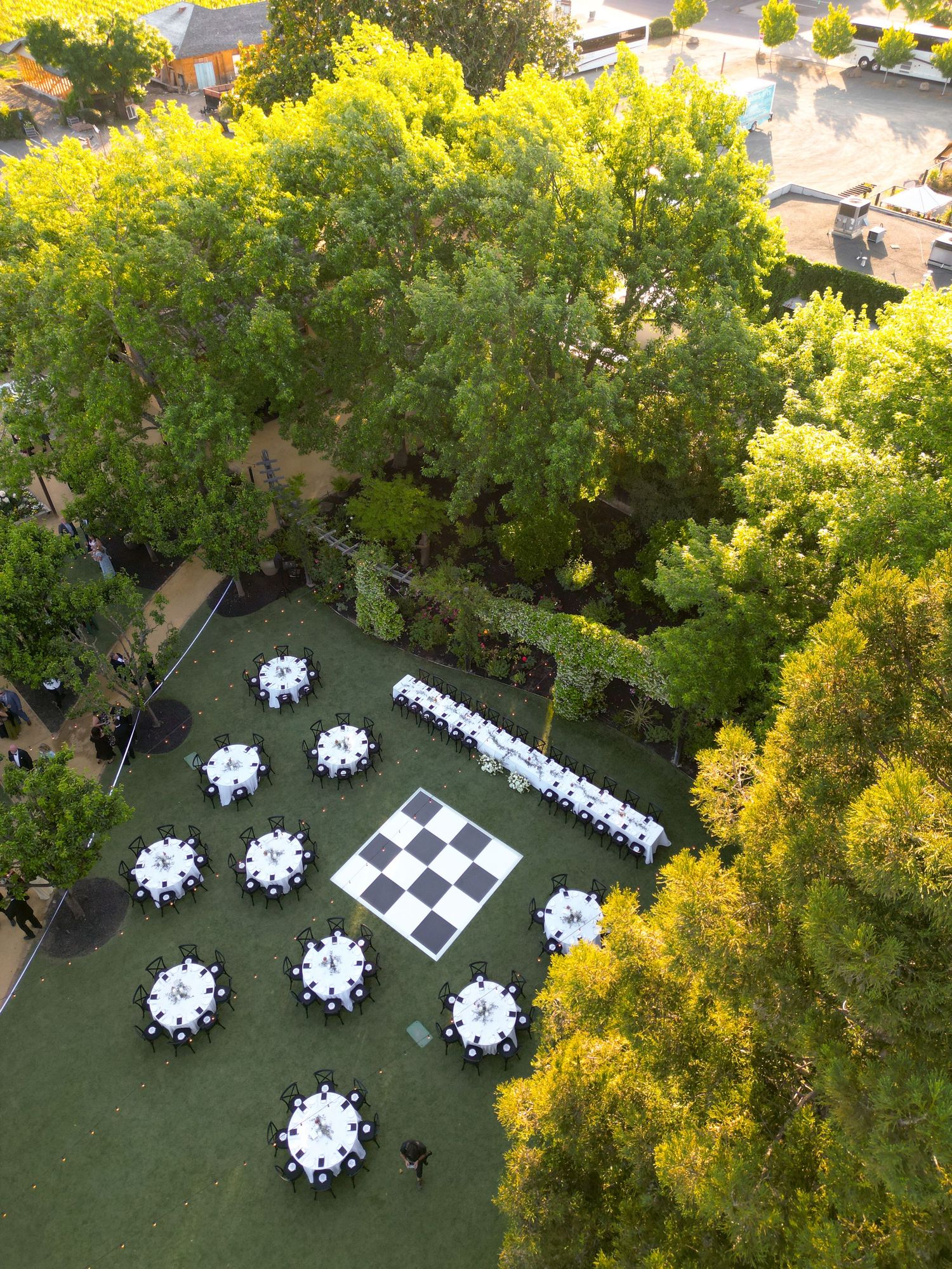 Aerial view of outdoor wedding reception with round tables, long banquet table, and black and white dance floor.